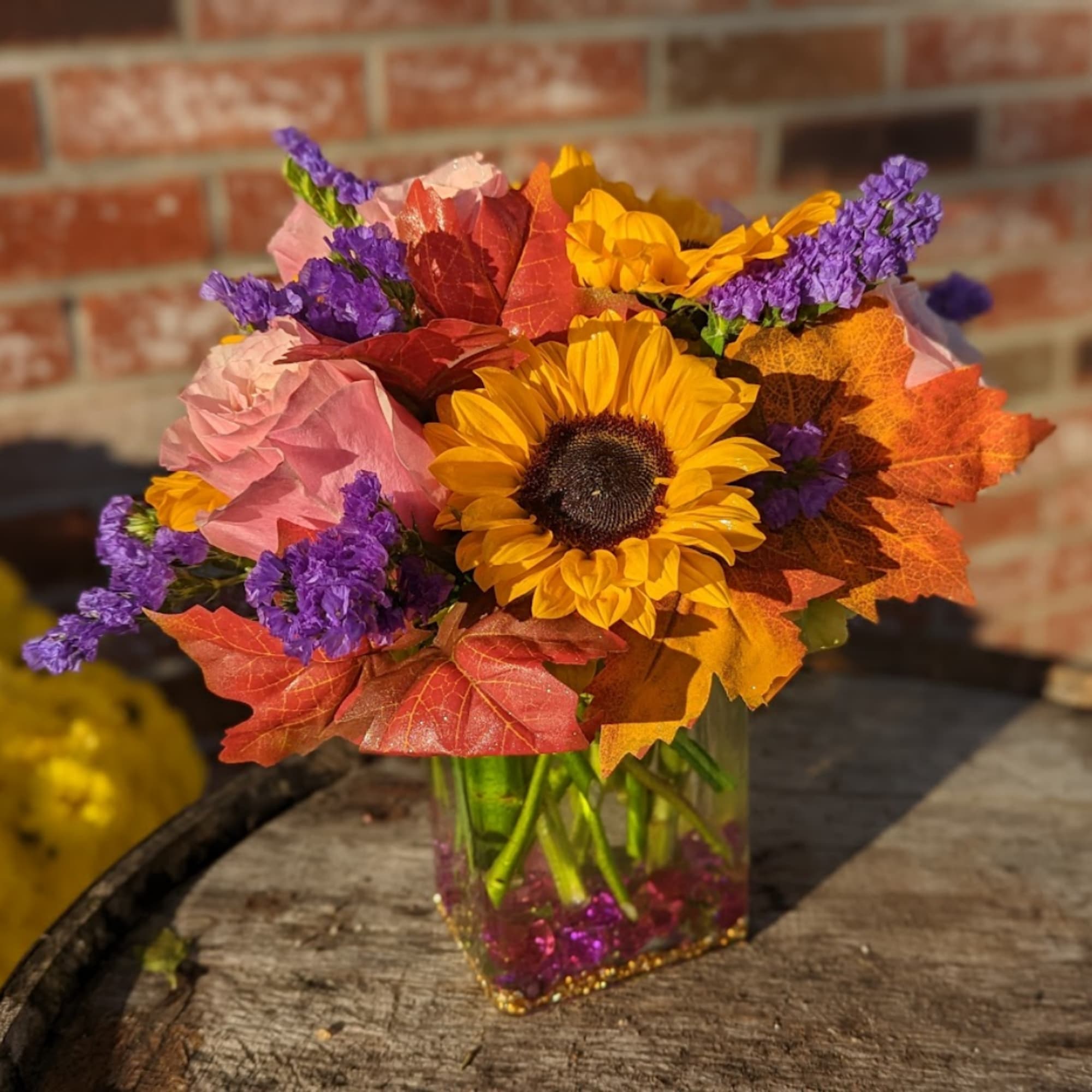 Sunflower bouquet with autumn leaves in a clear square vase