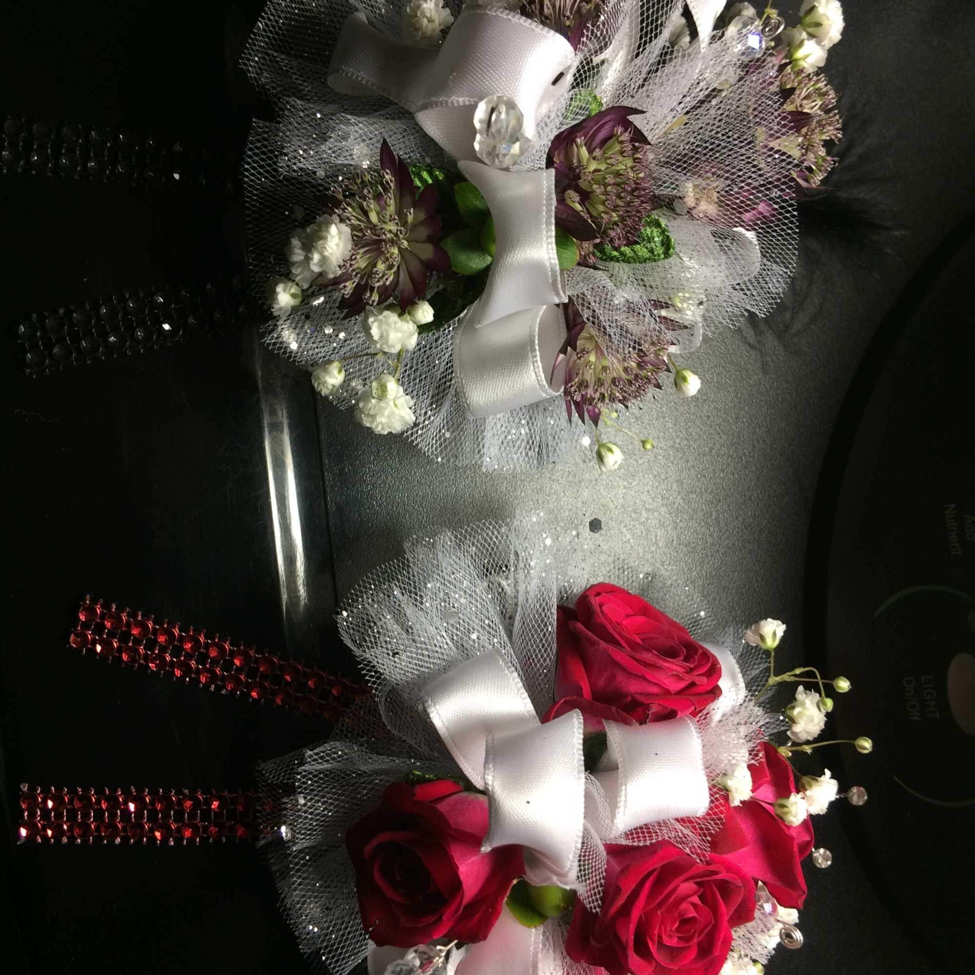 Two small floral corsages with roses and white ribbon on black packaging.