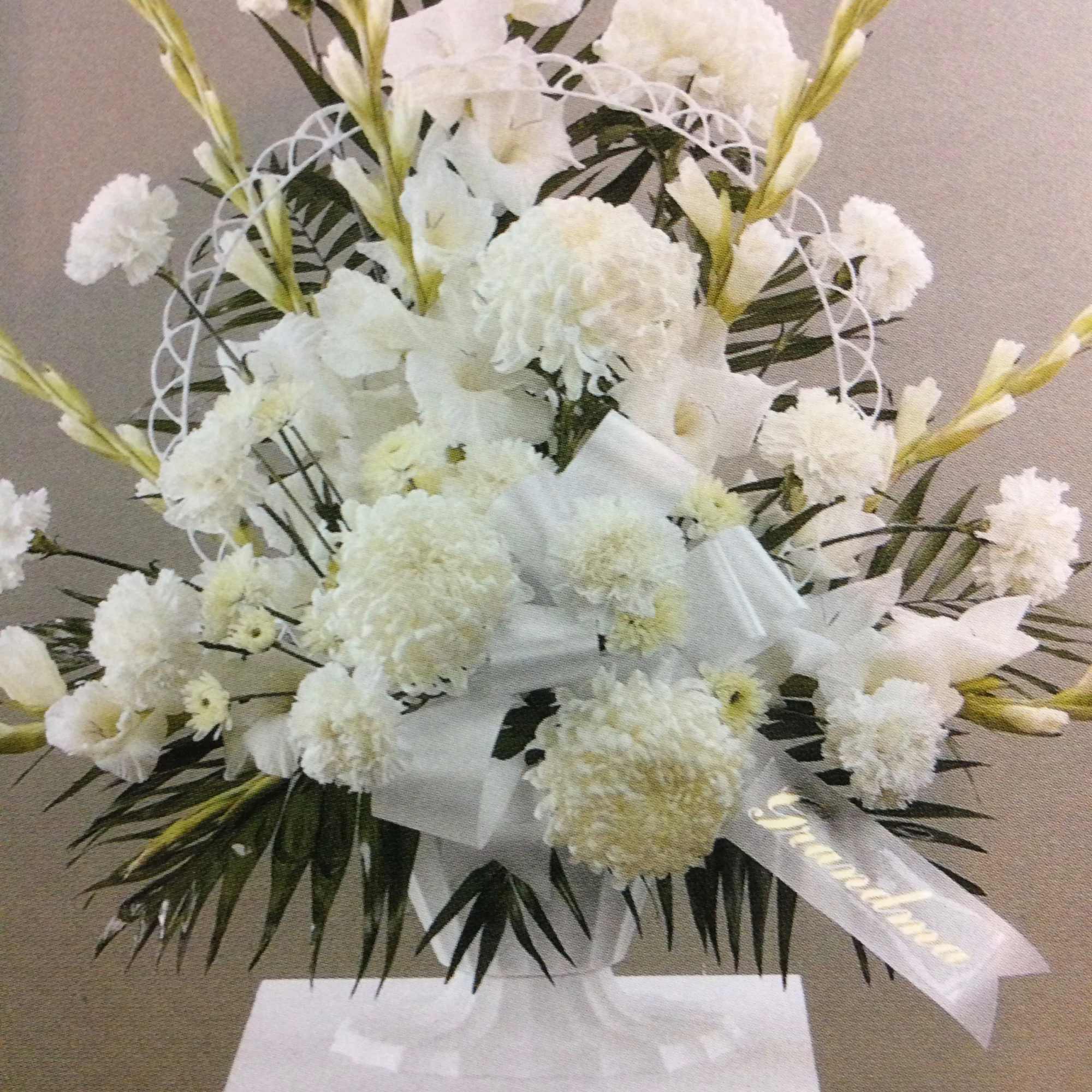 White floral standing arrangement with ribbon on a pedestal