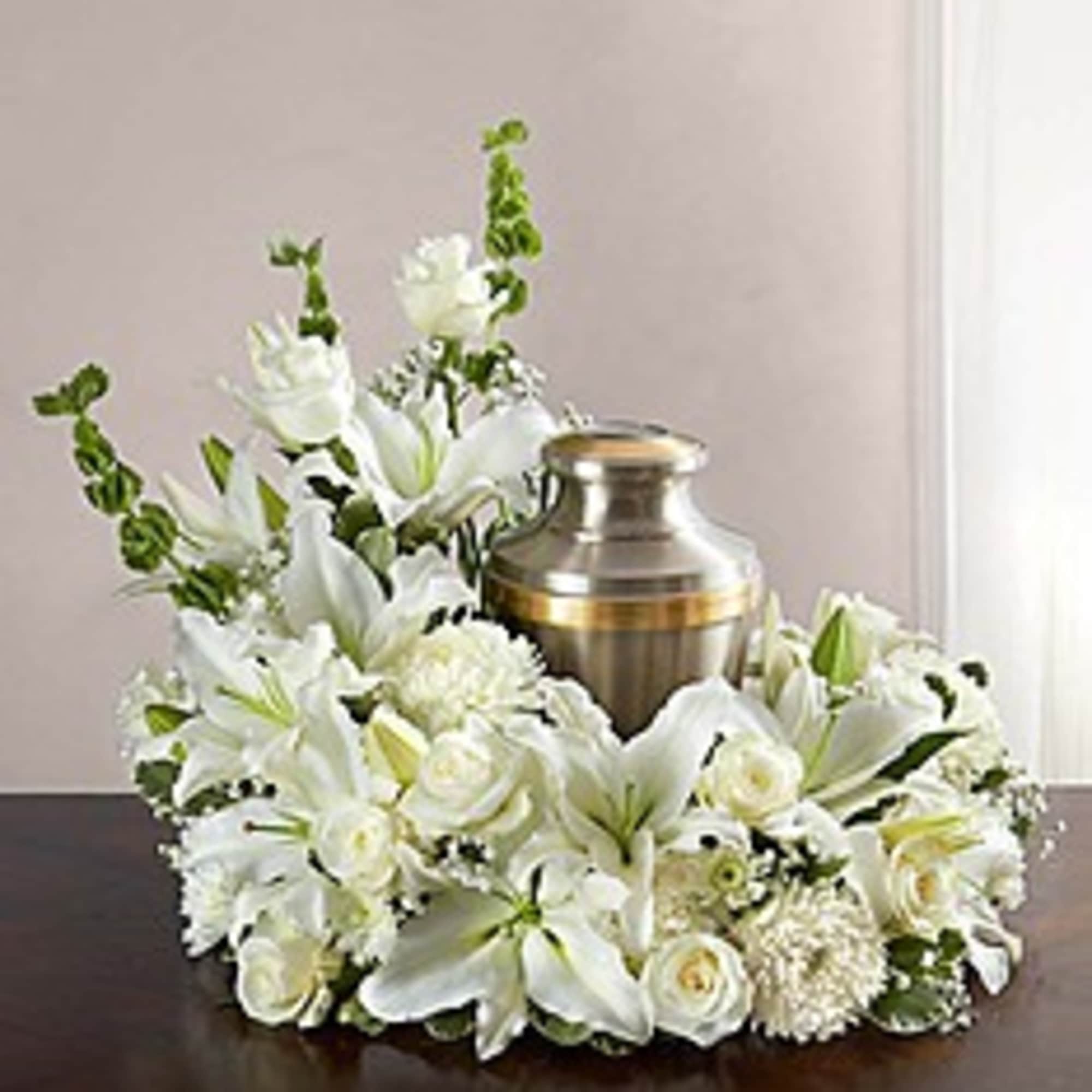 White floral funeral wreath around a brass urn