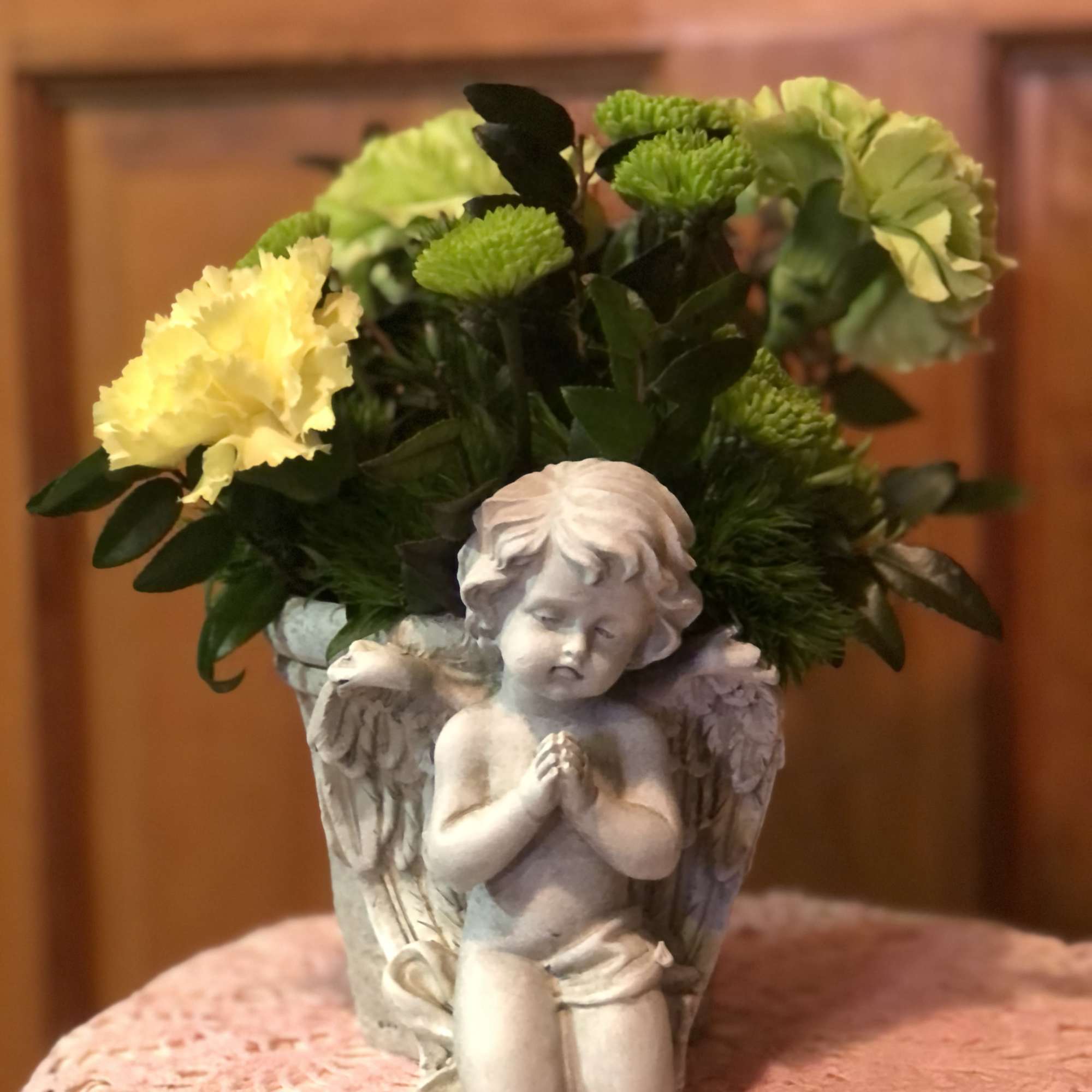 Yellow carnations and green mums in an angel-themed pot with a kneeling cherub figure