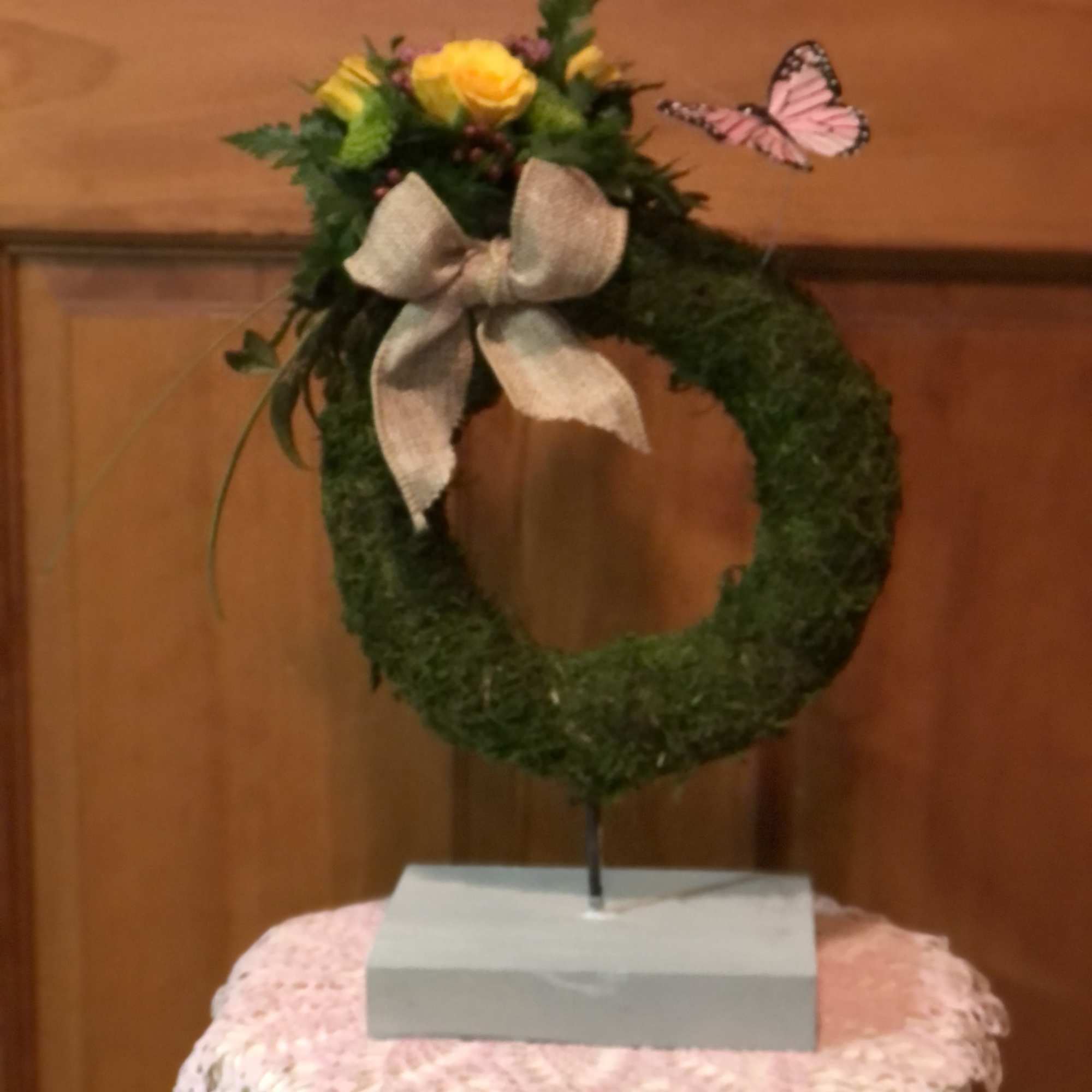 Moss wreath with yellow flowers, a bow, and a pink butterfly topper