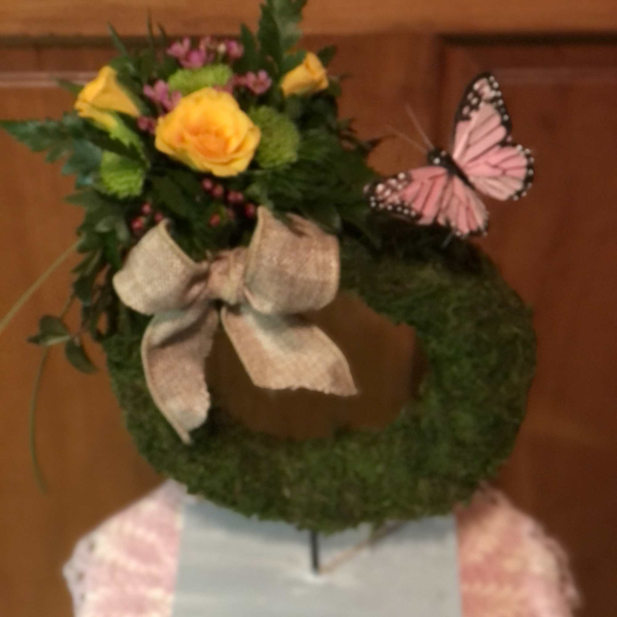 Moss wreath with yellow roses, pink flowers, and a butterfly decoration