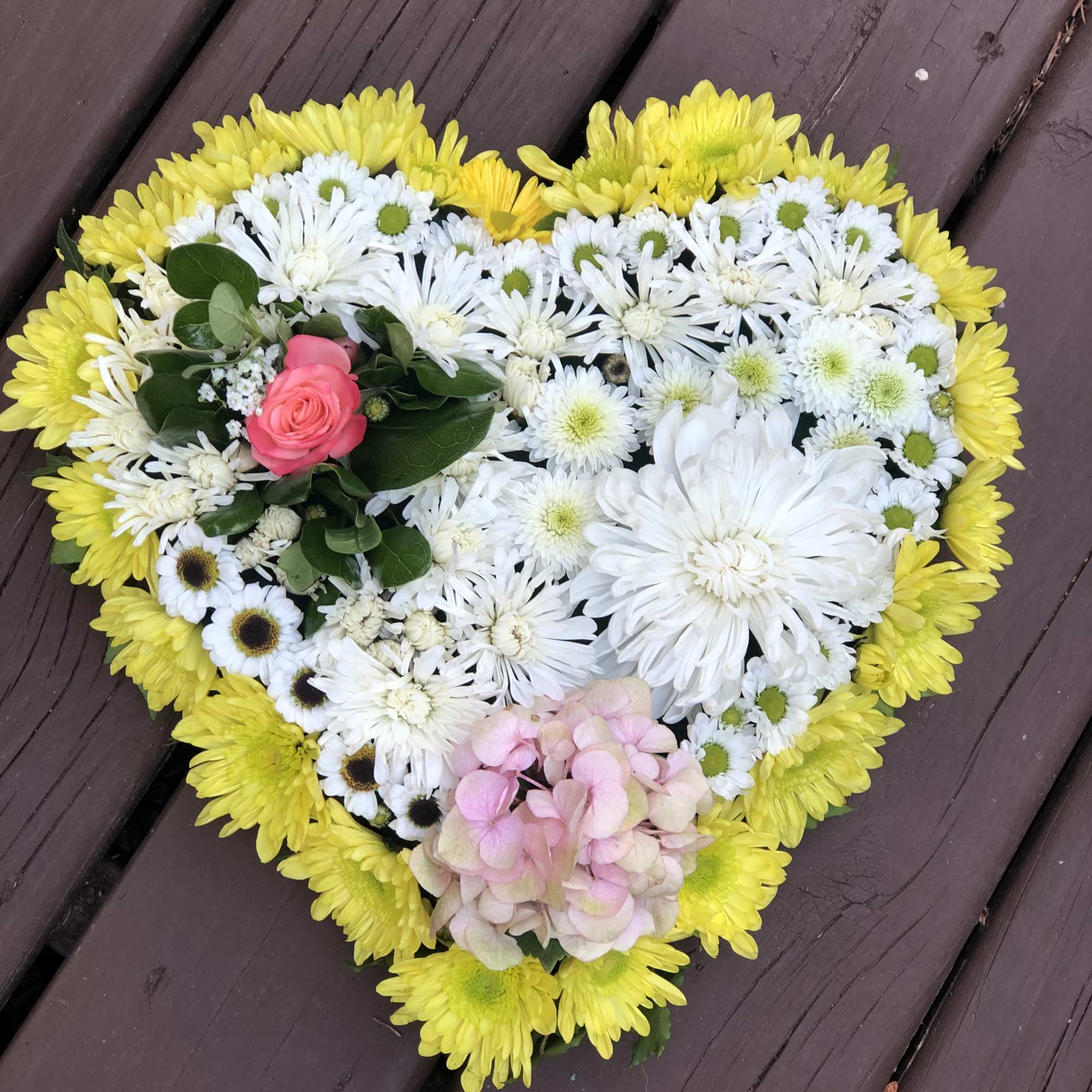 Heart-shaped floral arrangement with yellow, white, pink, and green blooms