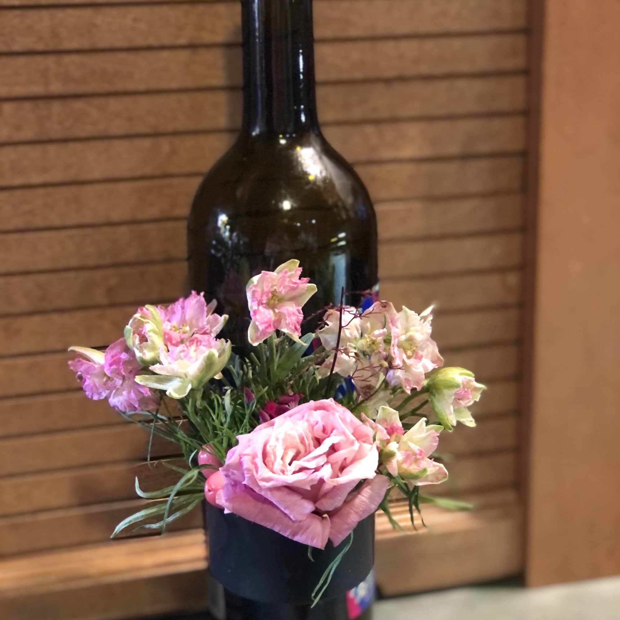 Pink rose and small pink flowers arranged on a wine bottle