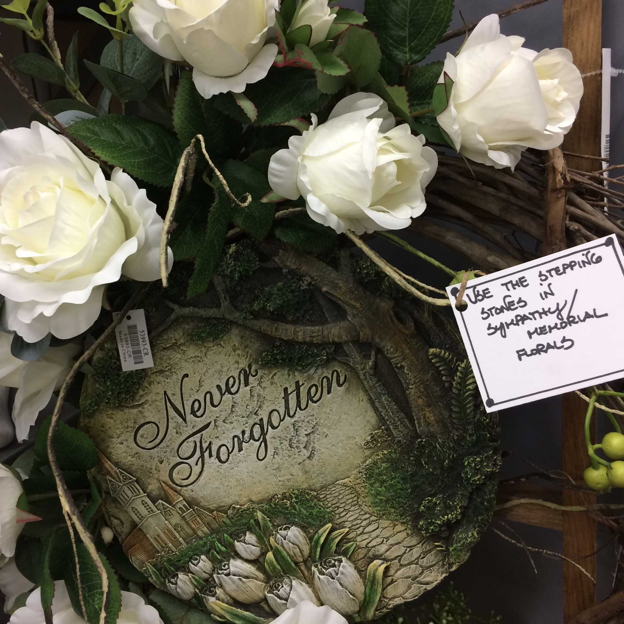 White roses arranged around a memorial stone with greenery