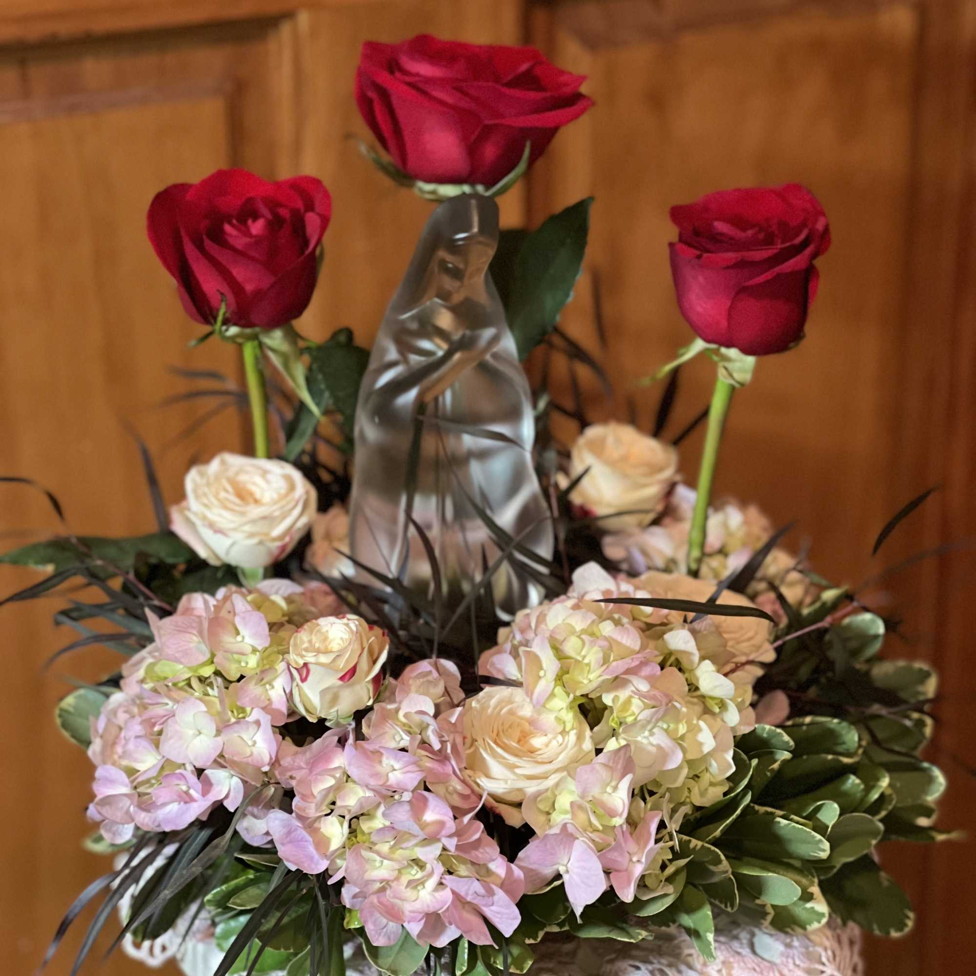 Red roses and pale pink hydrangeas arranged around a clear figurine in a vase