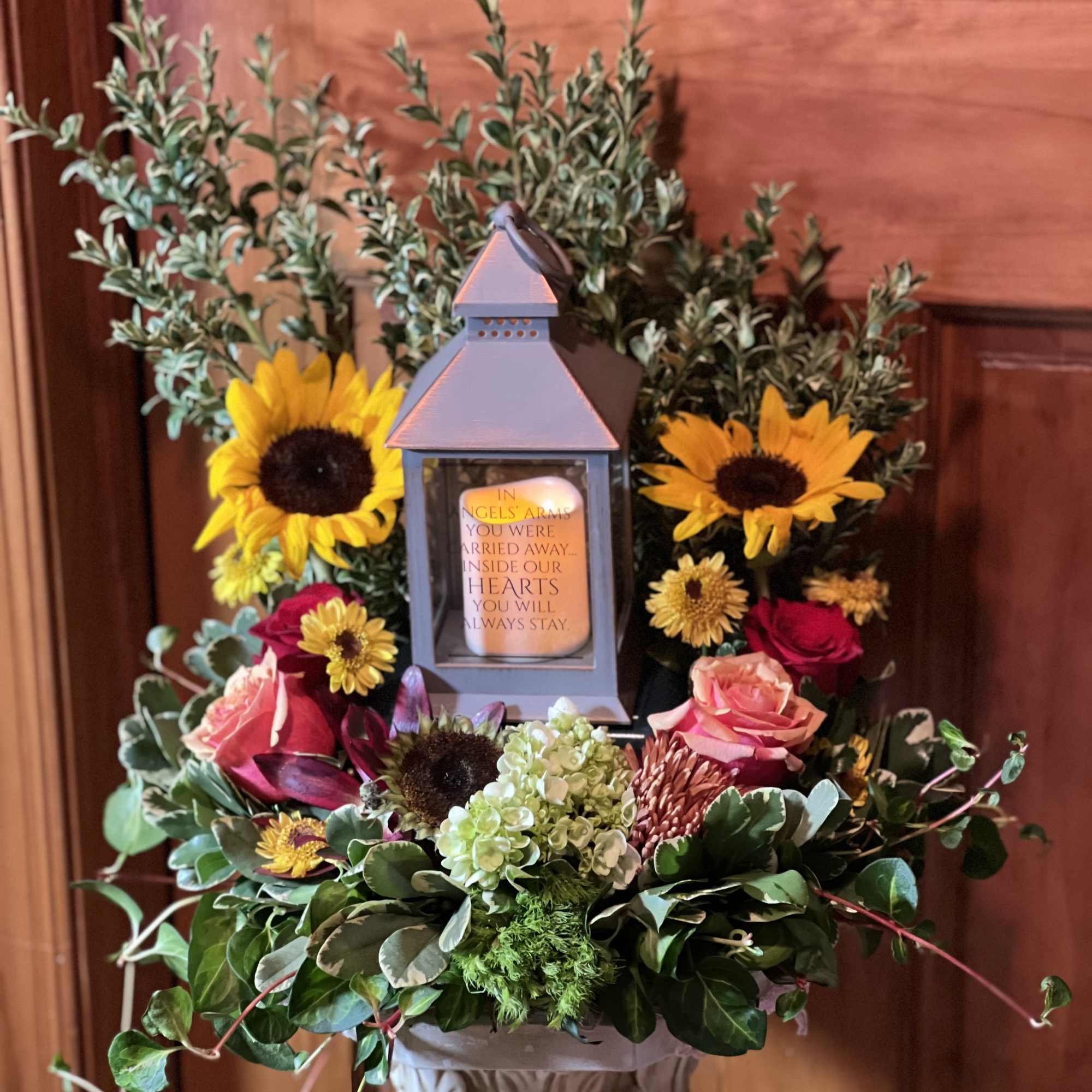 Sympathy floral arrangement with sunflowers, roses, and a lantern centerpiece