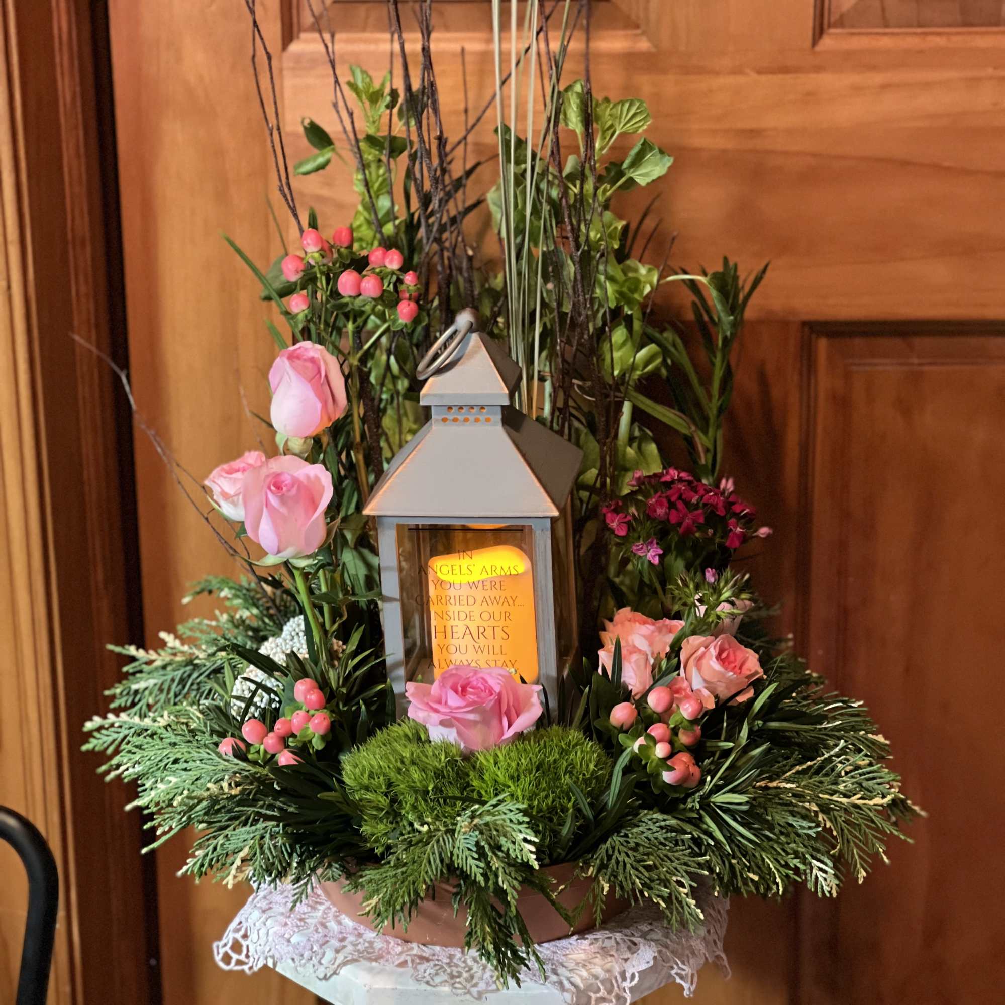 Pink roses and berries arranged around a lantern on a pedestal.