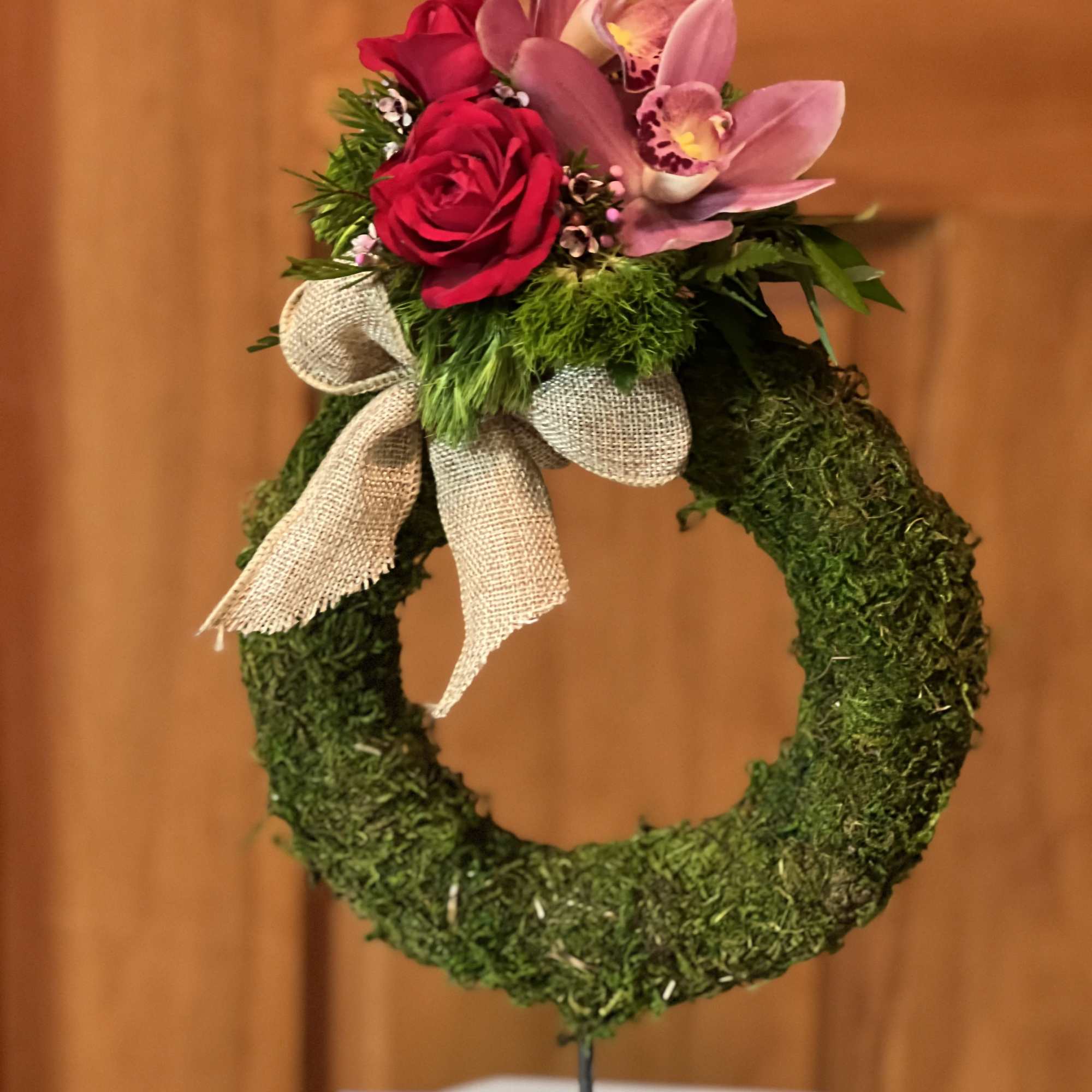 Moss wreath with pink orchids, red roses, and a burlap bow
