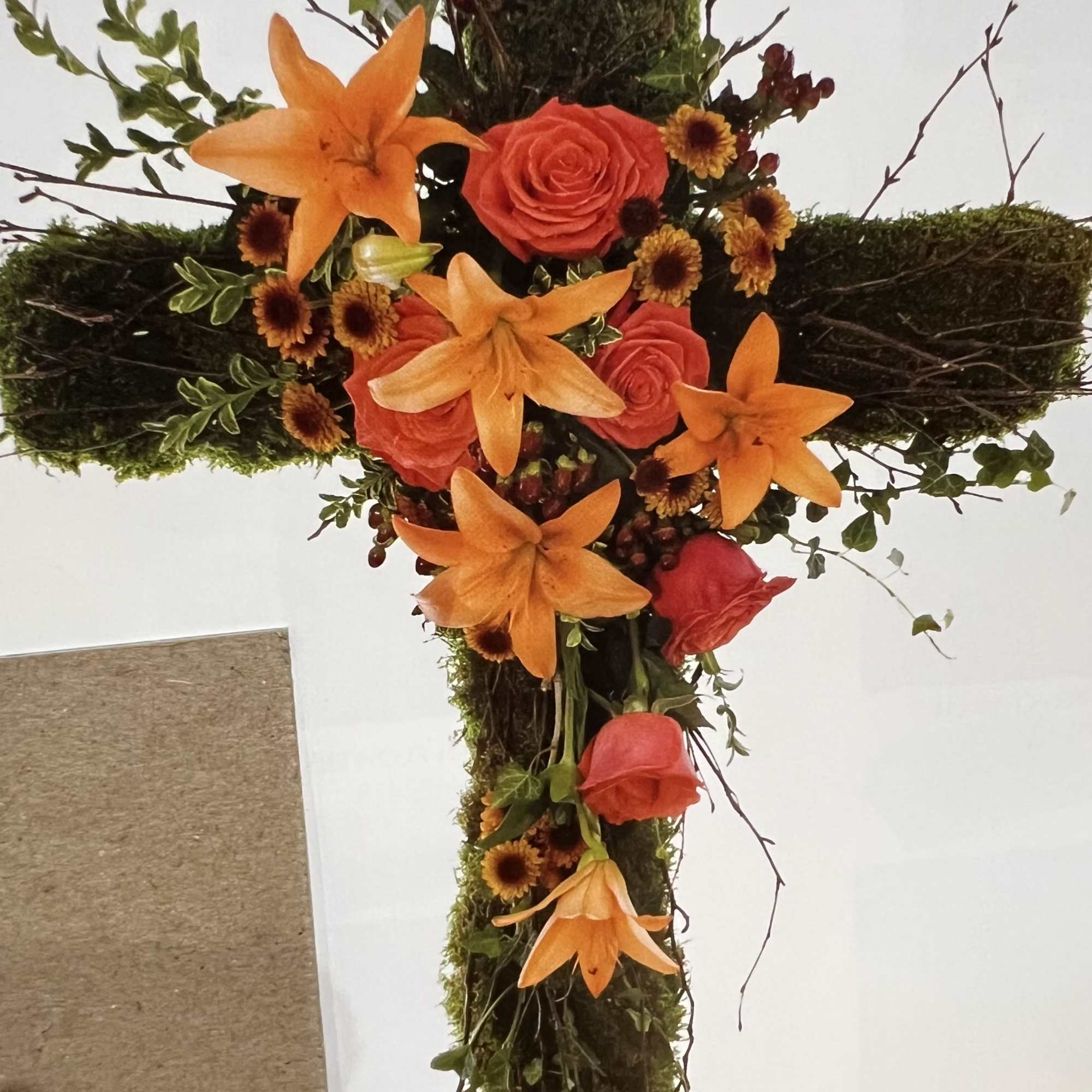 Cross-shaped floral arrangement with orange lilies and coral roses