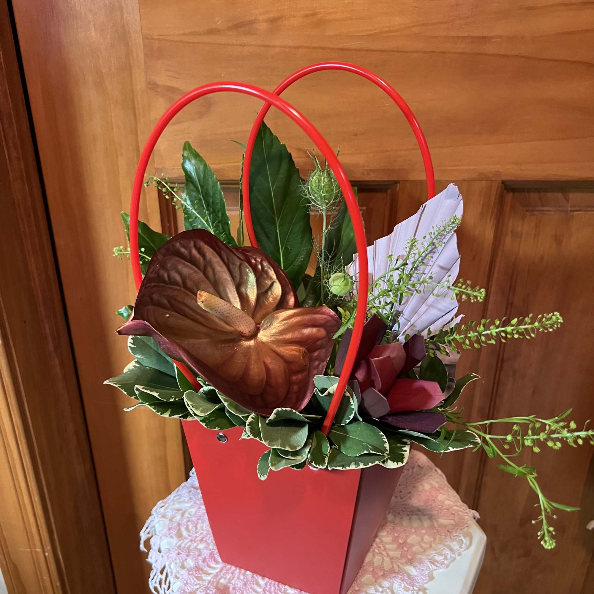 Red gift basket with anthurium blooms and greenery on a lace-covered stand