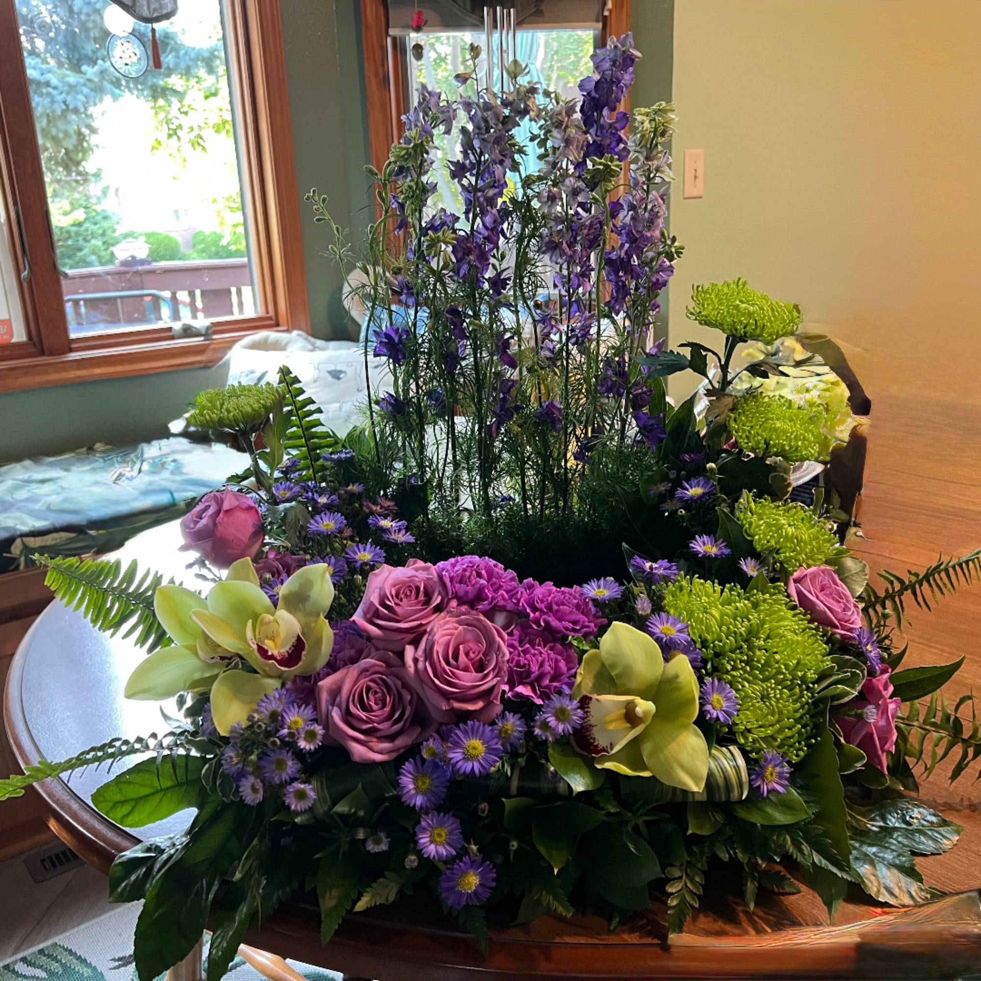 Large floral centerpiece with purple roses, green mums, and tall purple blooms