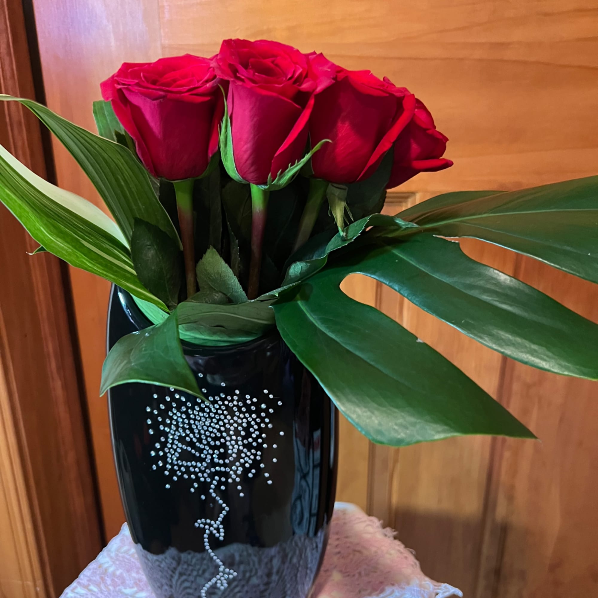 Red roses arranged in a black vase with broad green leaves.