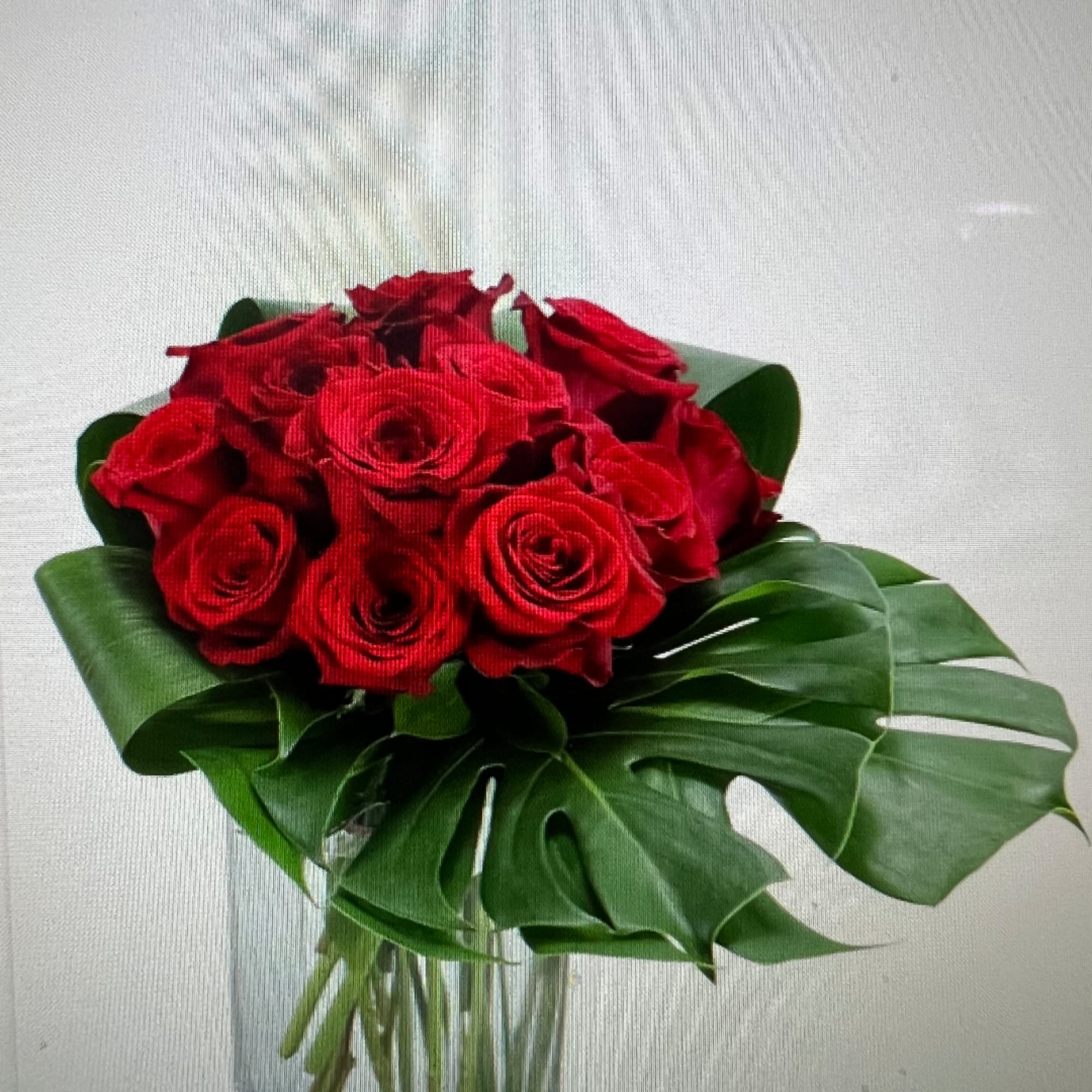 Bouquet of red roses with large tropical leaves in a clear vase
