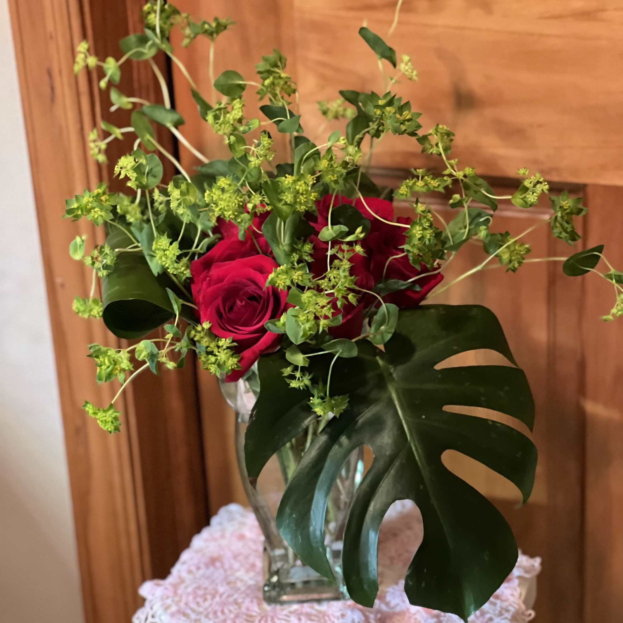 Red roses in a glass vase with green filler and large split leaves