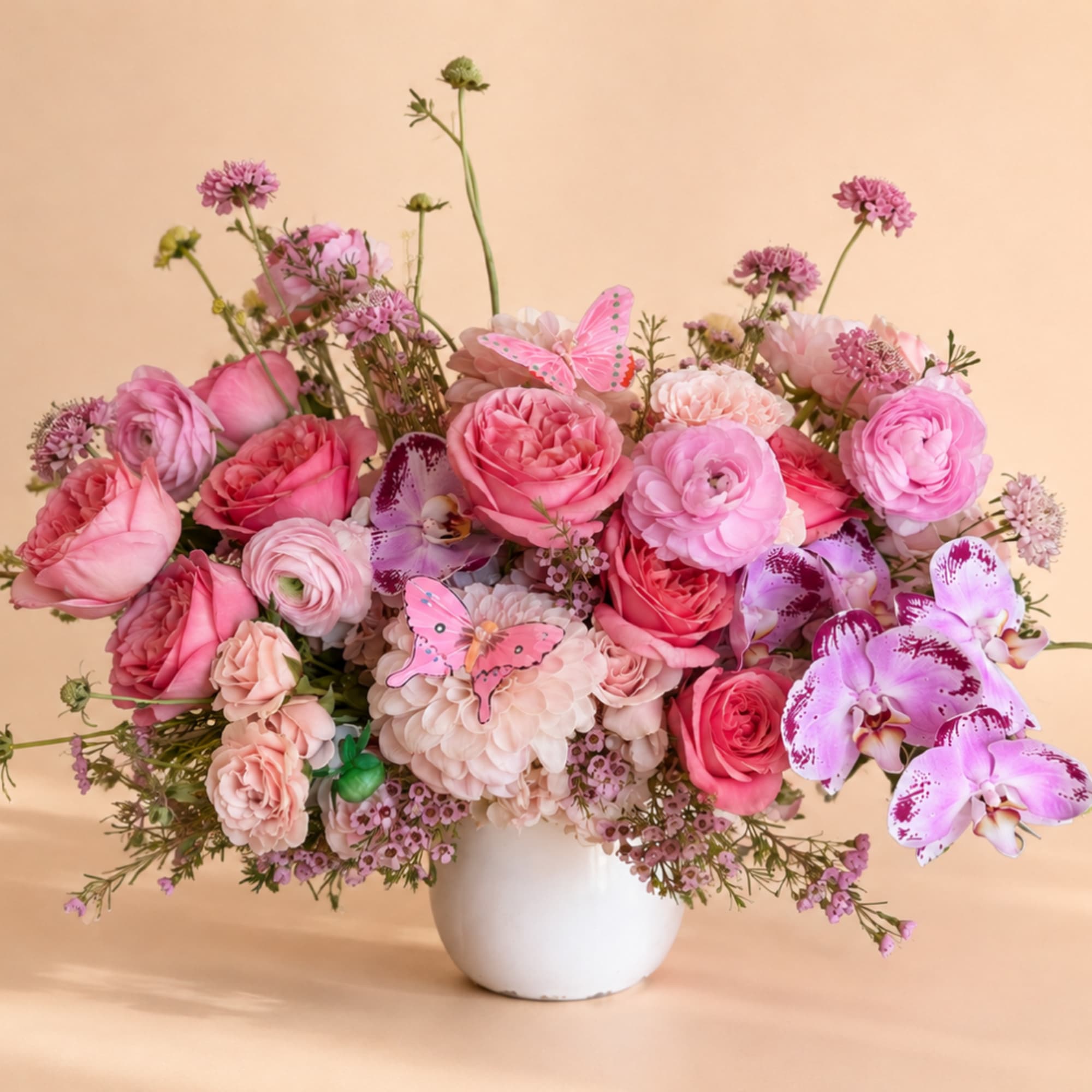 Pink and lavender flower arrangement in a white vase with butterfly accents