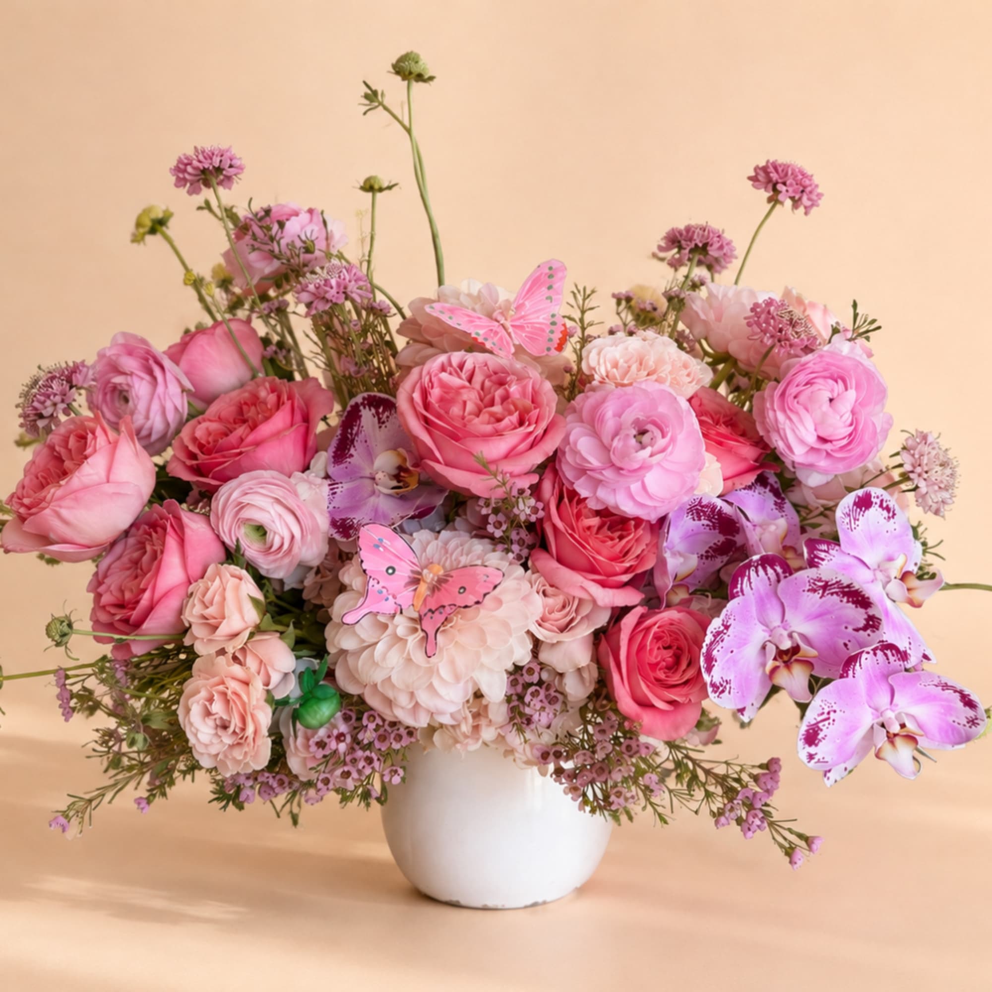 Pink mixed flower arrangement in a white vase with butterfly picks