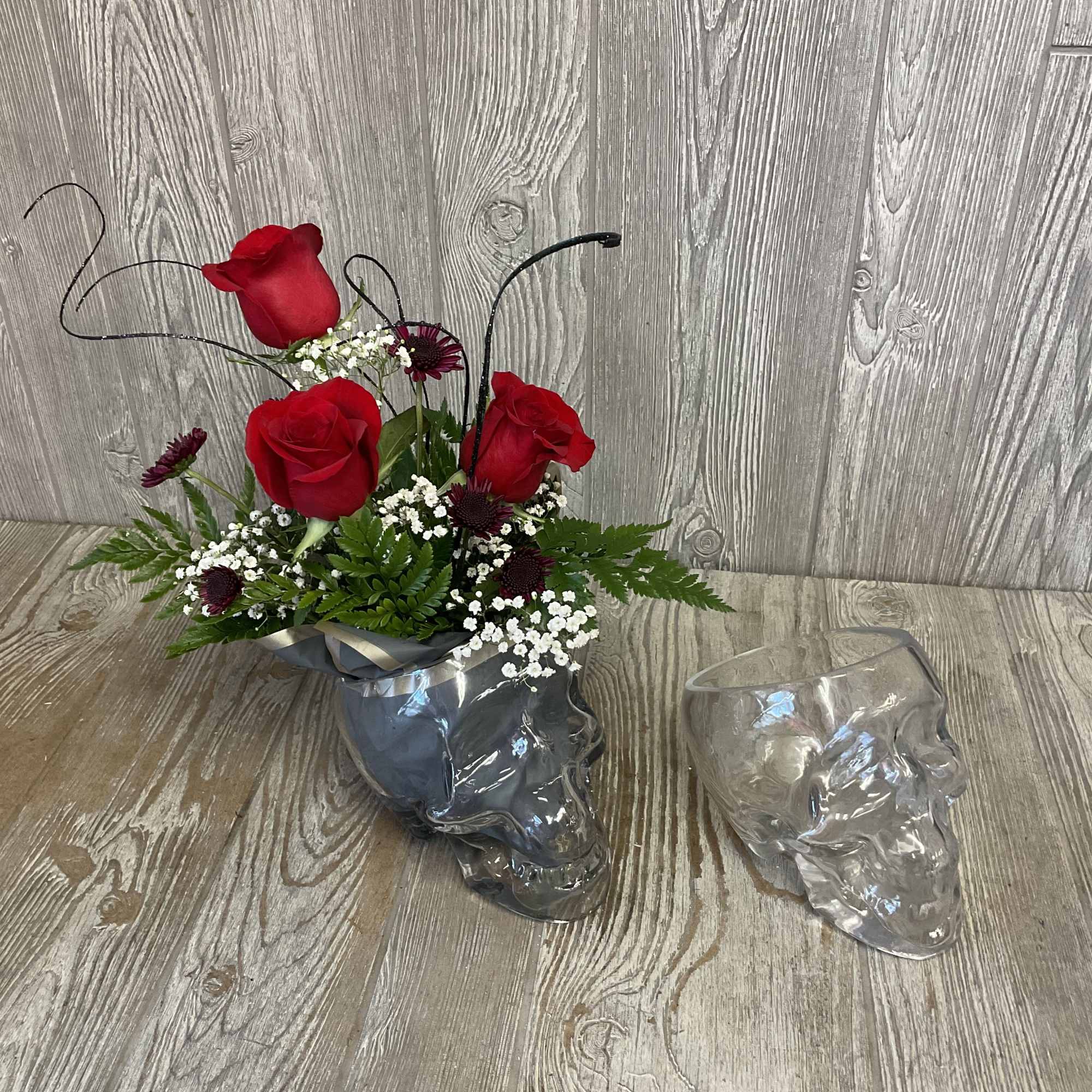Red roses arranged in a clear skull-shaped vase with white filler flowers