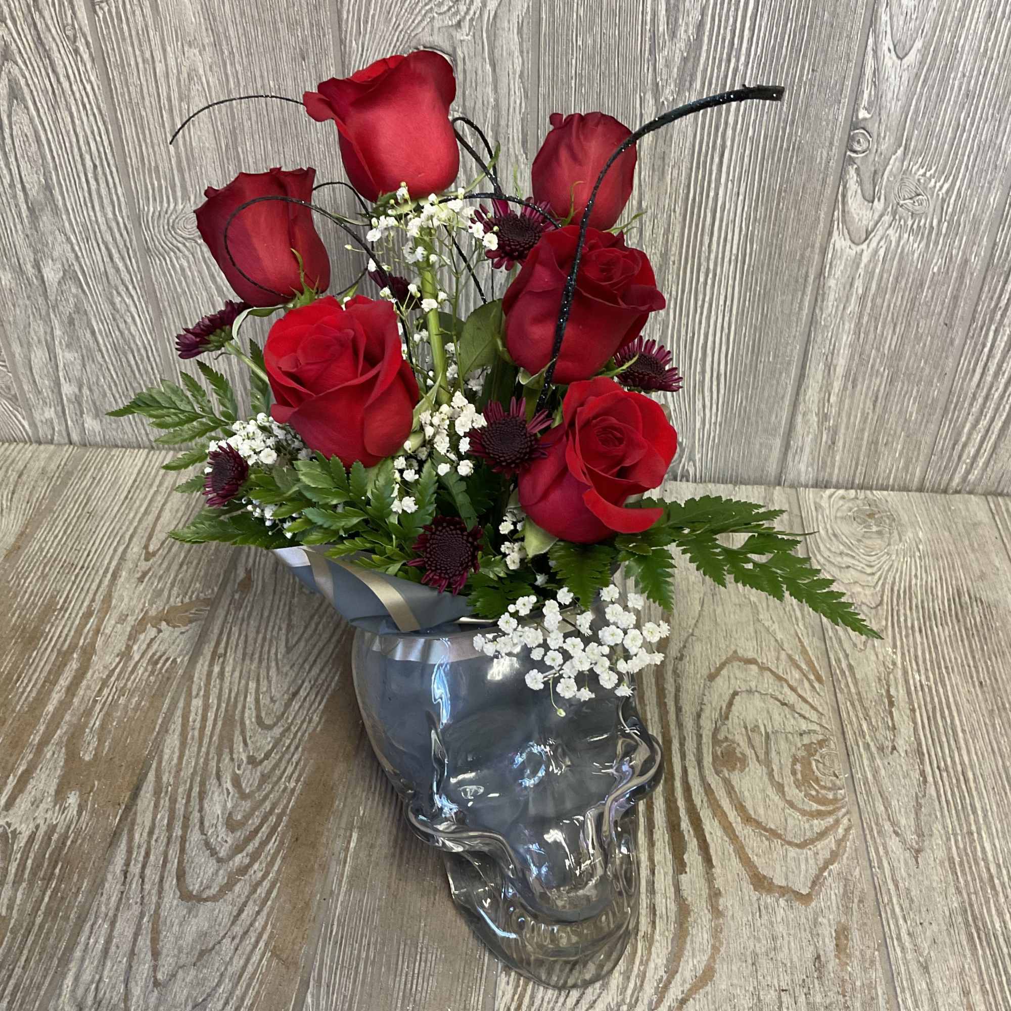 Red roses arranged in a clear skull-shaped vase with white filler flowers