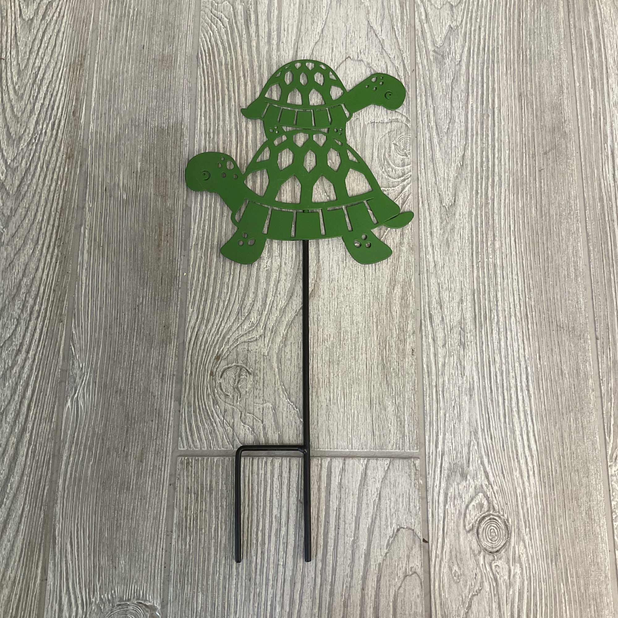 Green metal turtle garden stake on a wood floor