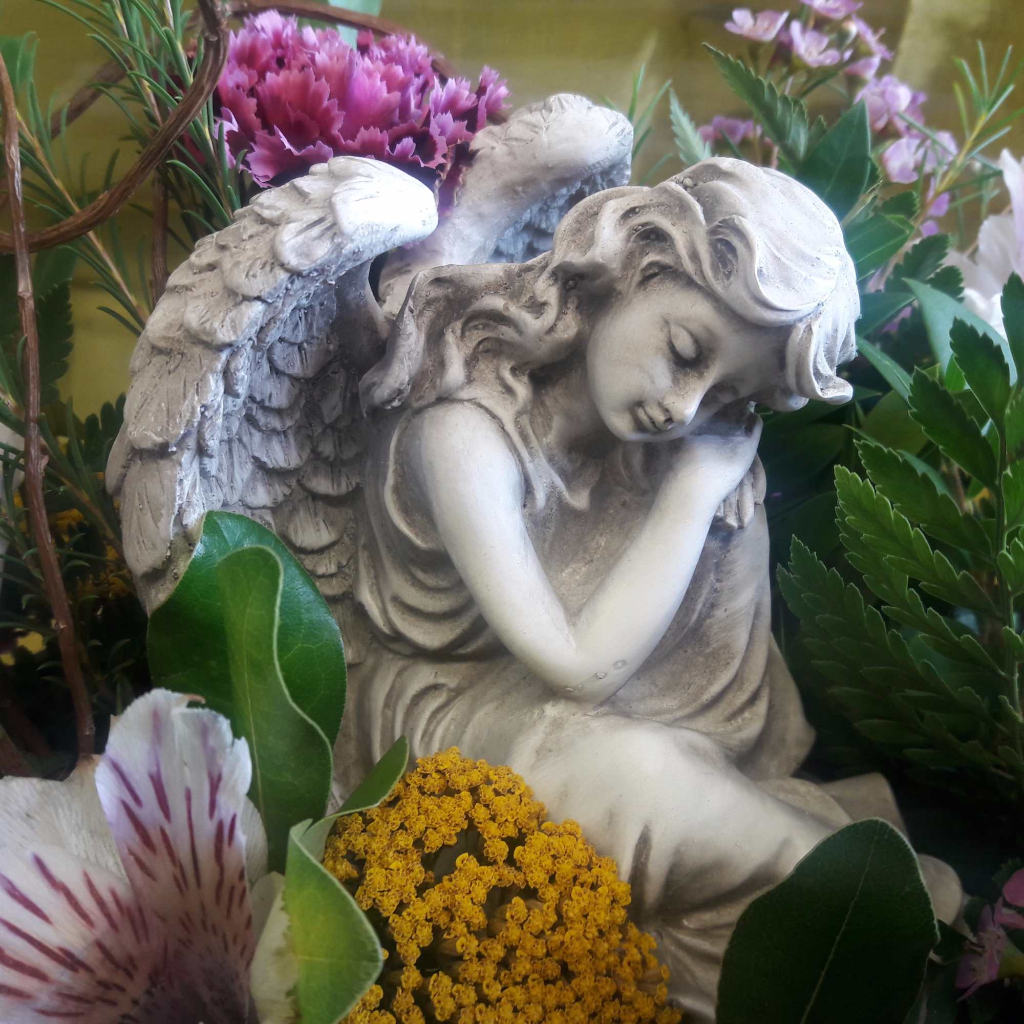 Angel figurine surrounded by mixed flowers and greenery