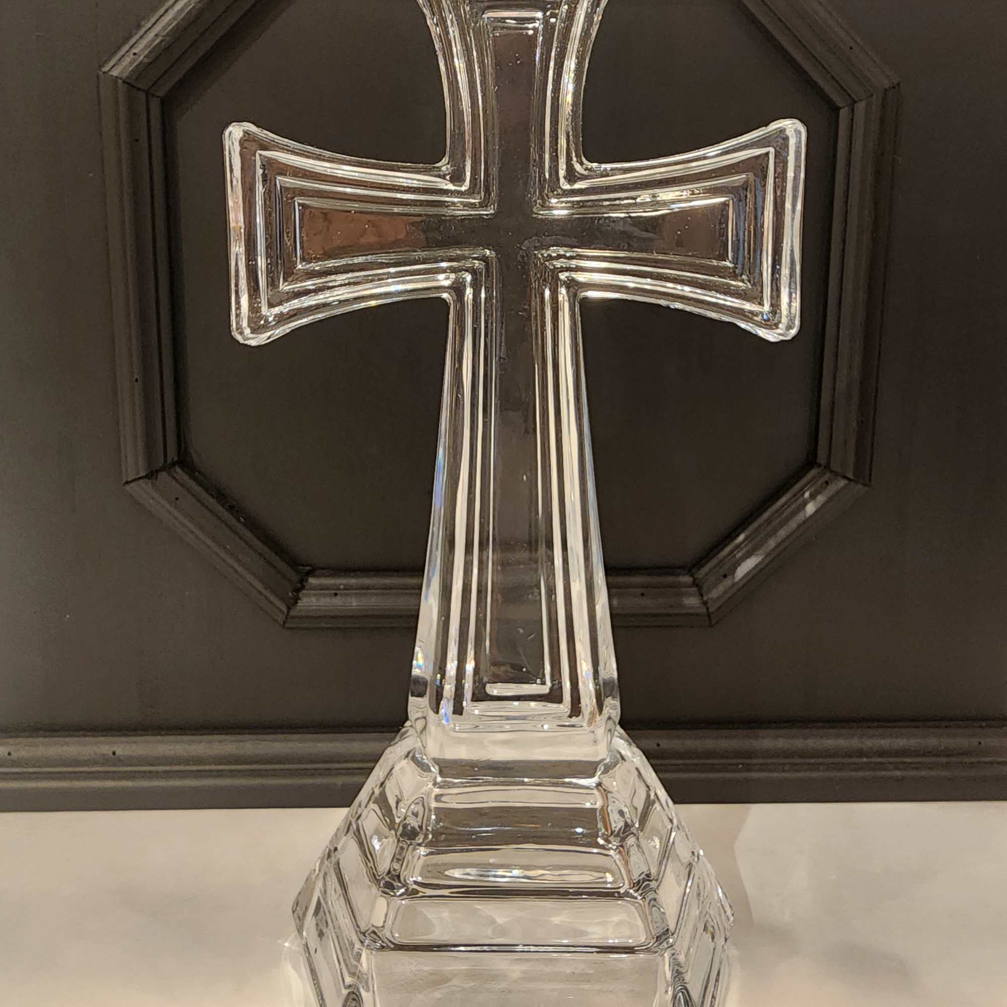 Clear glass cross-shaped decorative piece on a dark background