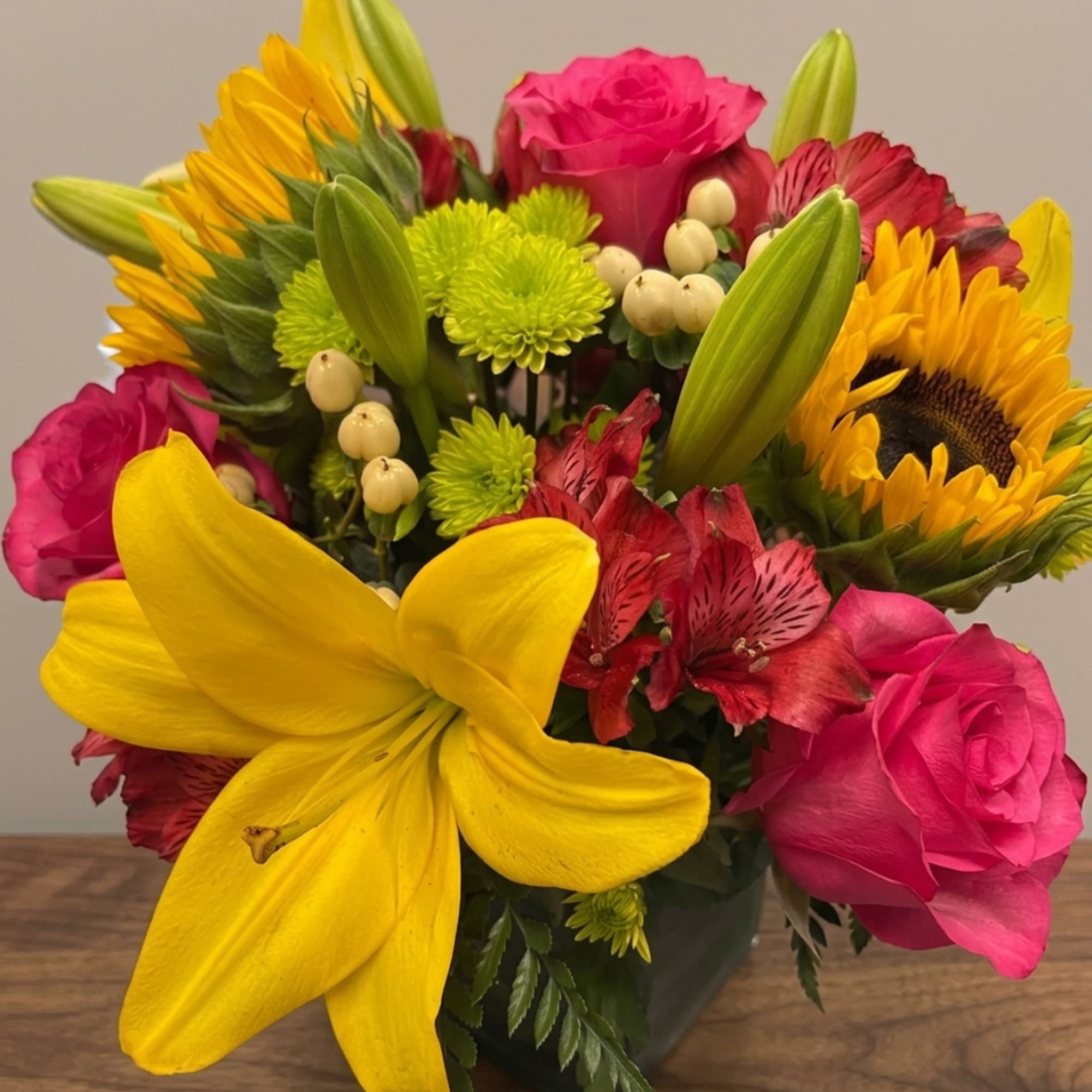 Bright mixed bouquet with pink roses, sunflowers, and a yellow lily in a vase