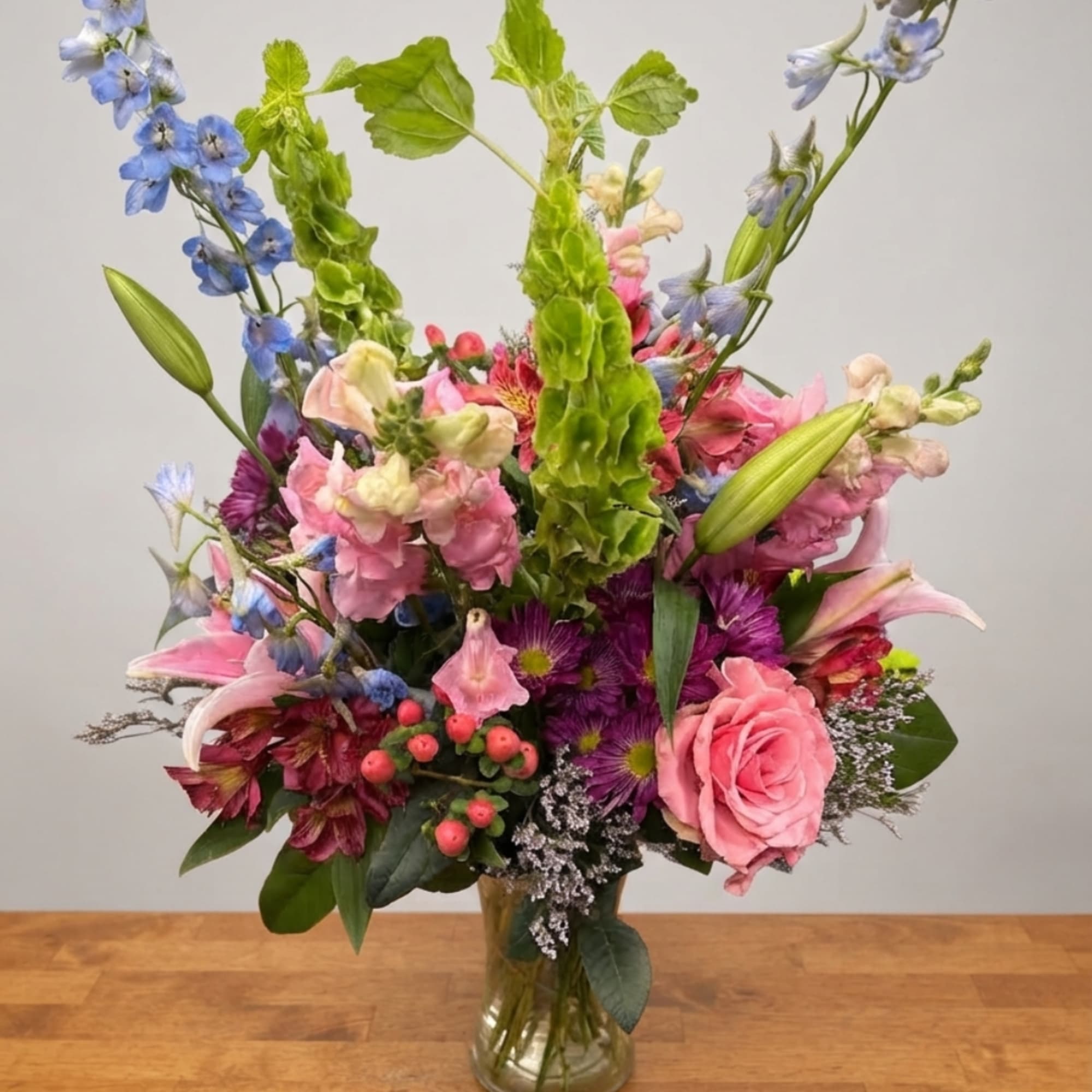 Mixed bouquet of pink, blue, and purple flowers in a clear glass vase