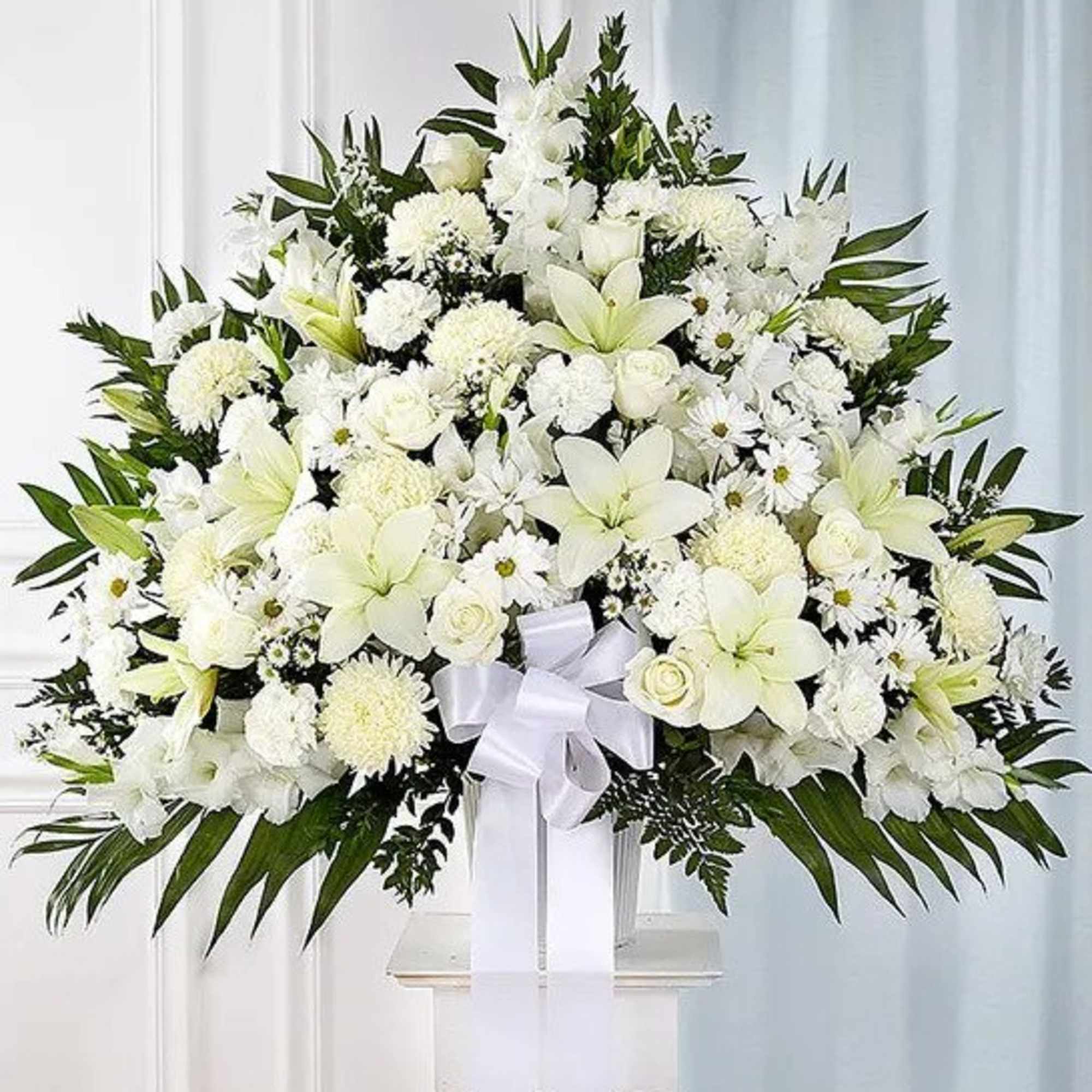 Large fan-shaped white lily and rose arrangement with a white bow on a pedestal