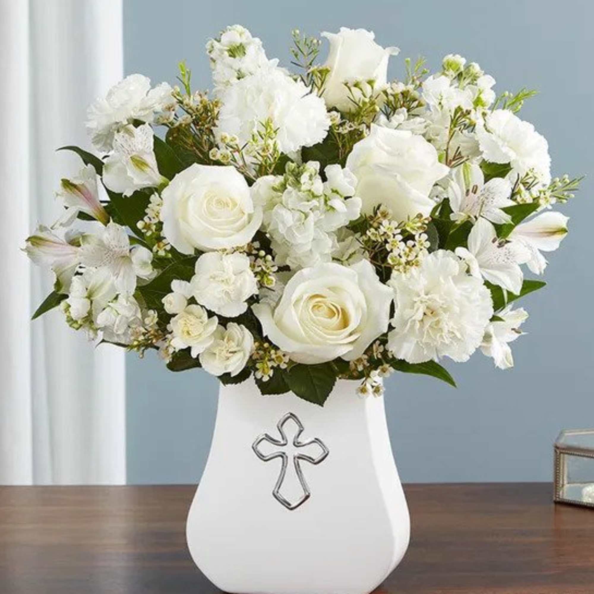 All-white flower arrangement in a white vase with a silver cross emblem