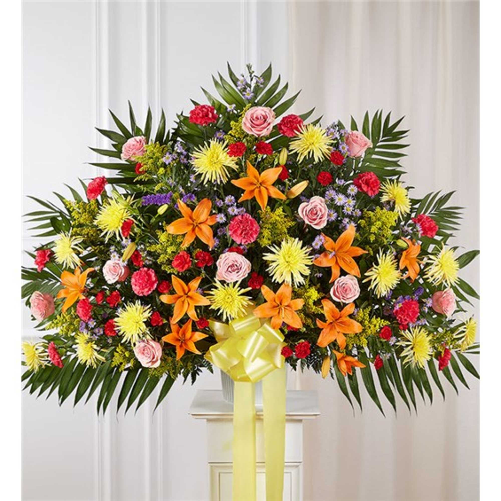 Large standing floral spray with yellow, orange, pink, and red flowers and a yellow bow.