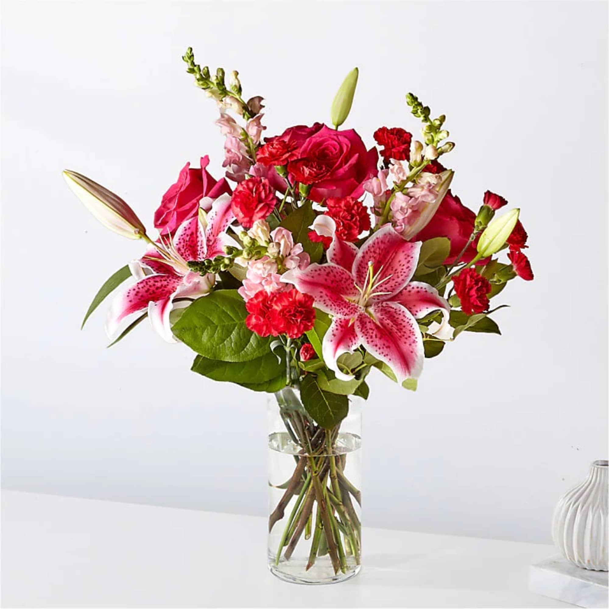 Pink lilies, red roses, and red carnations arranged in a clear glass vase with water