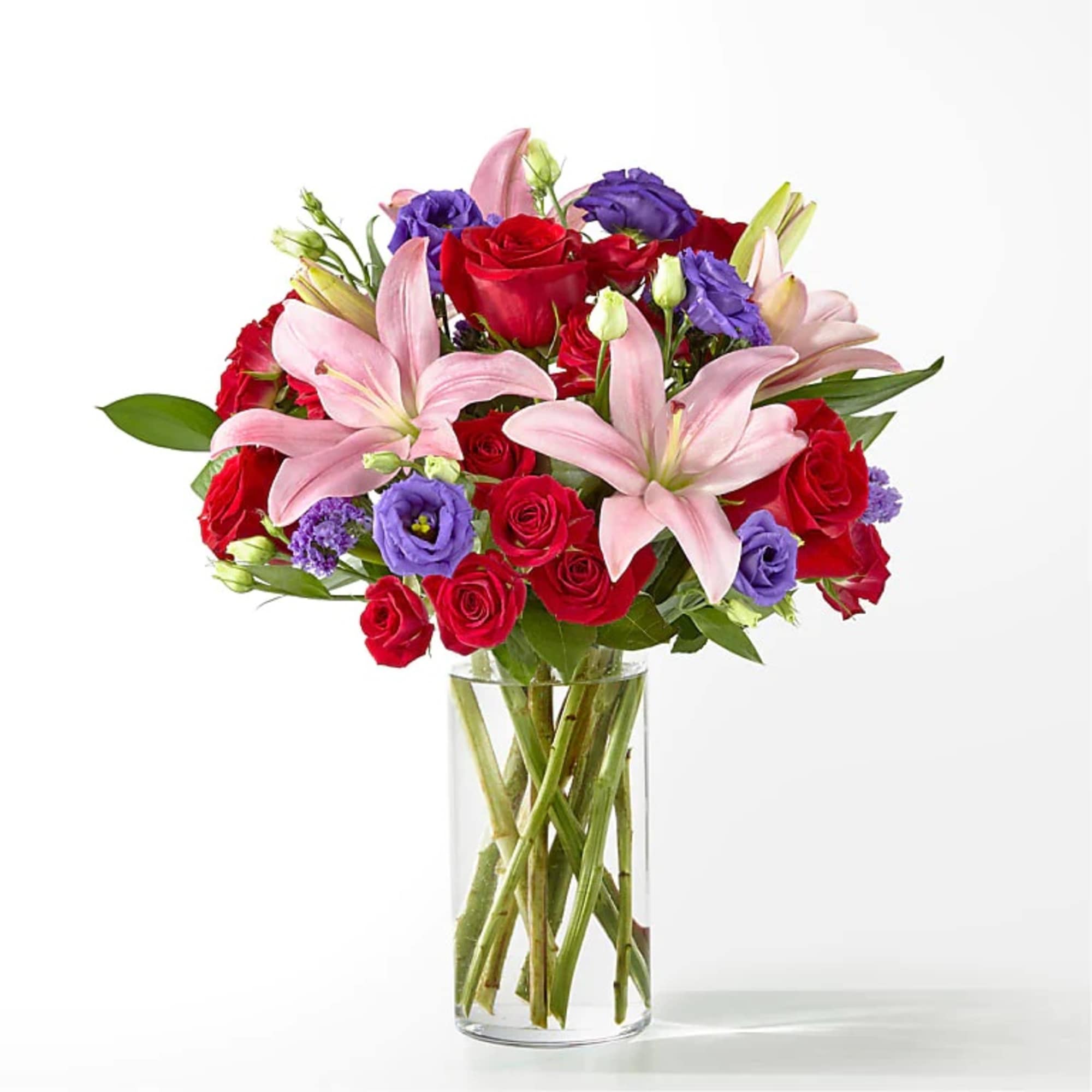 Mixed bouquet of pink lilies, red roses, and purple lisianthus in a clear glass vase.
