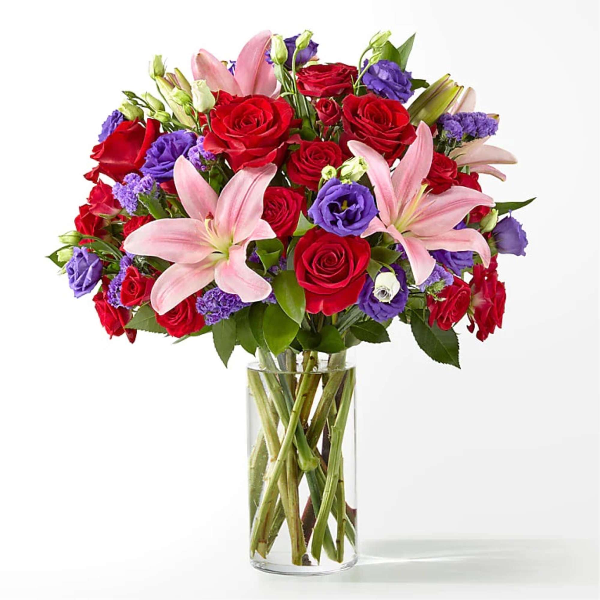 Mixed bouquet of red roses, pink lilies, and purple blooms in a clear glass cylinder vase