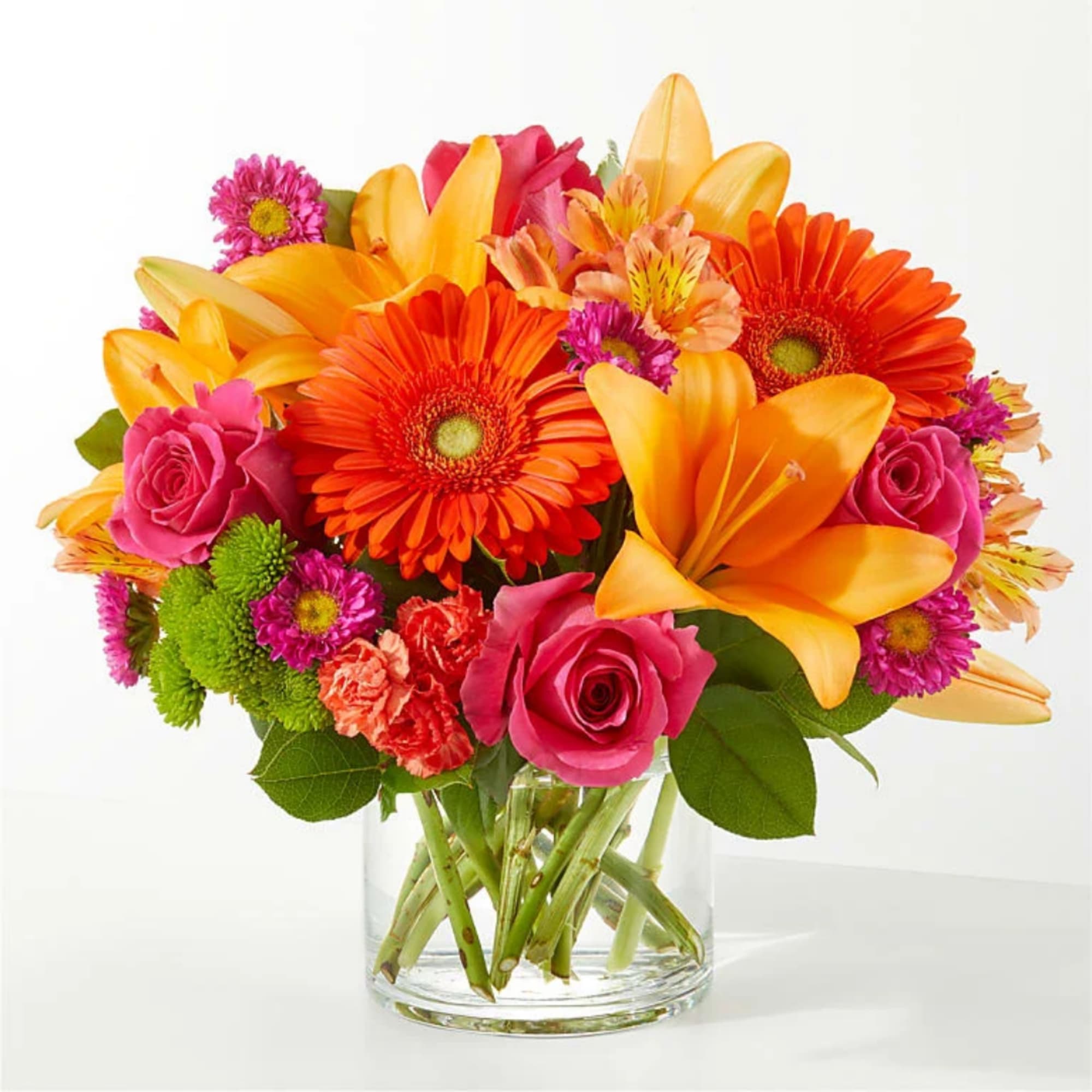 Bright mixed bouquet in a clear glass vase with orange lilies, gerbera daisies, and pink roses