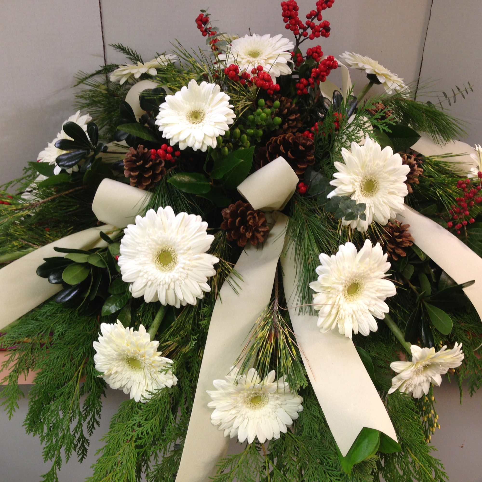 White gerbera daisy funeral spray with cream ribbons and pinecones
