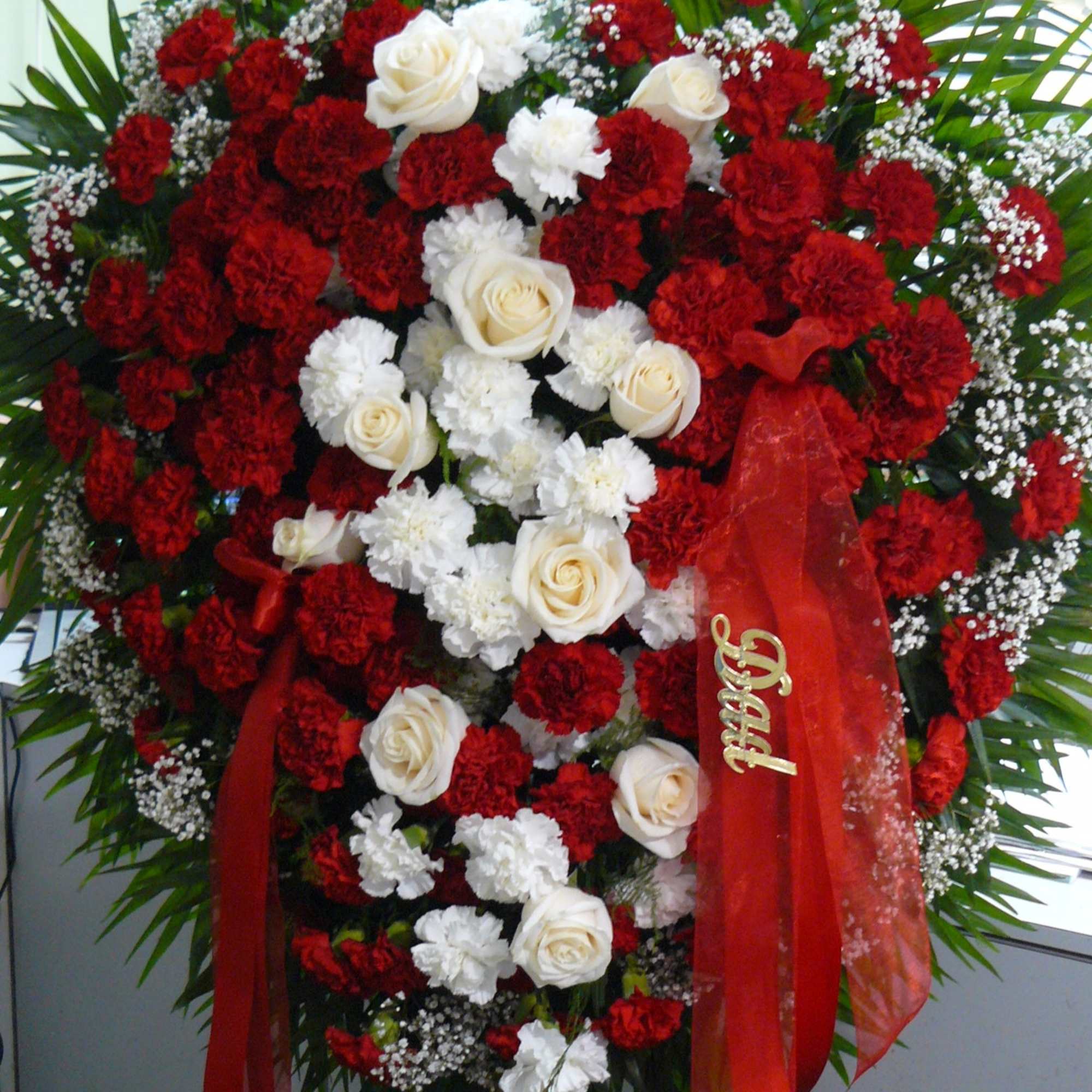 Large standing floral spray with red and white flowers and red ribbons
