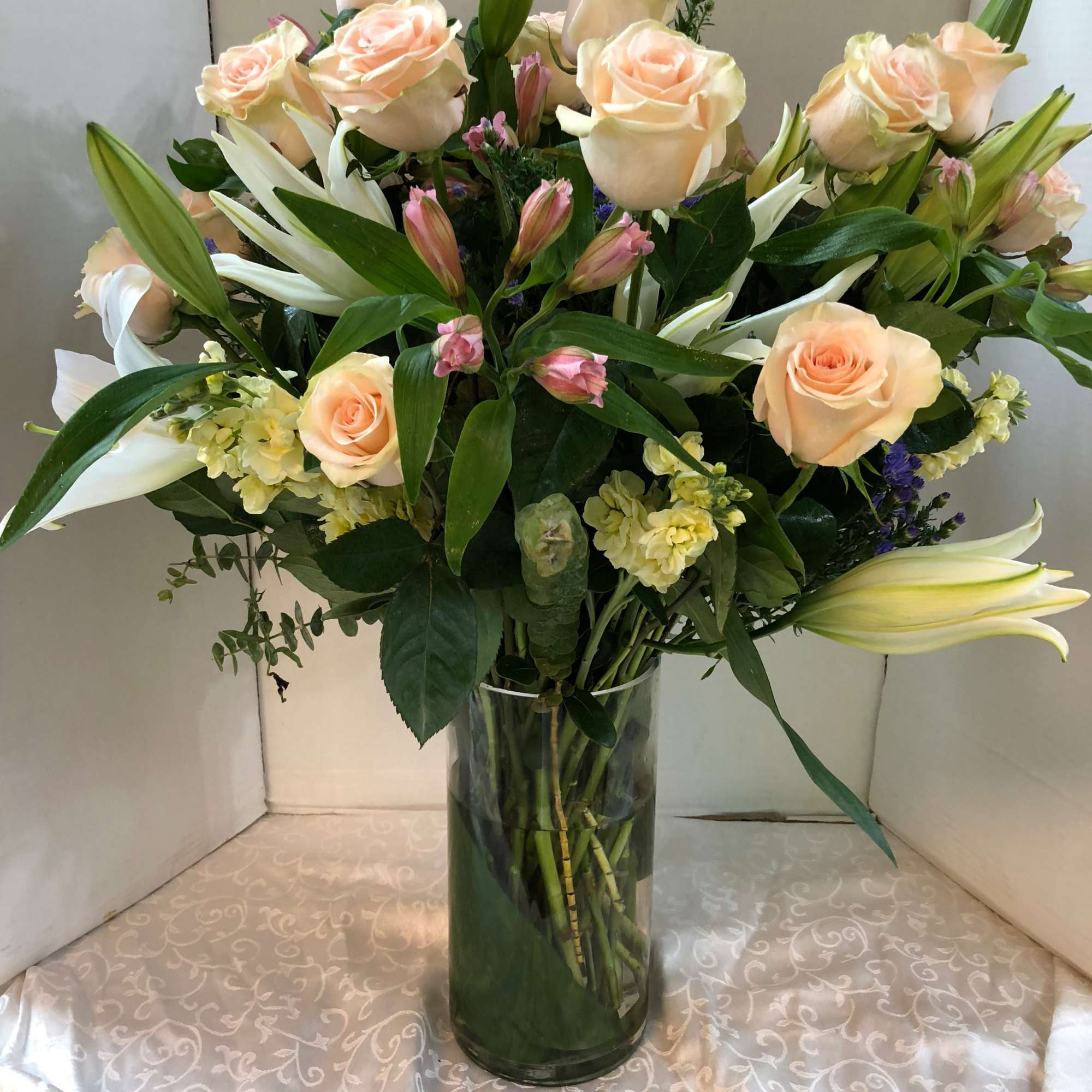 Peach roses and pure white hybrid lilies take center stage in this