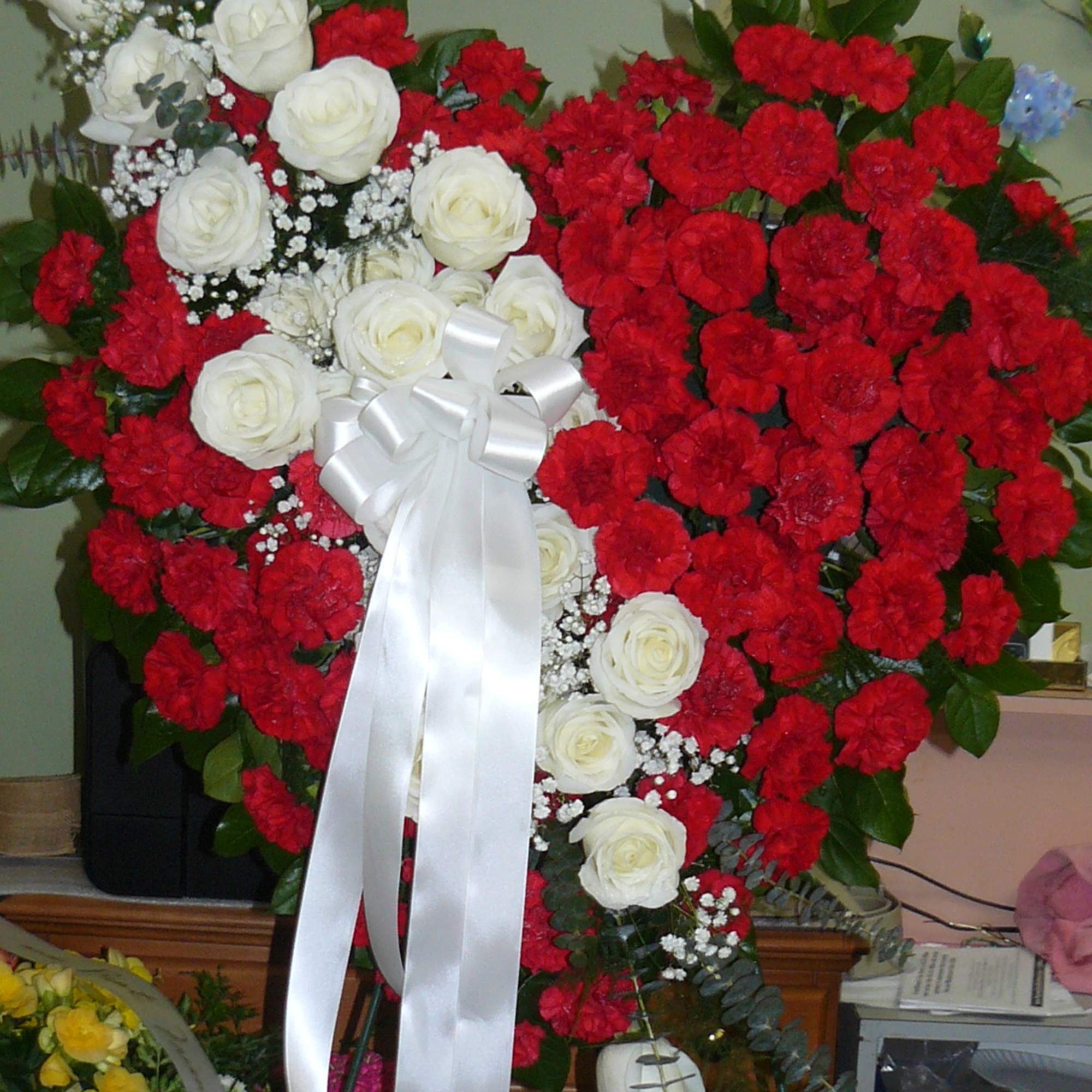 Heart-shaped floral spray with red carnations and white roses, tied with a white ribbon