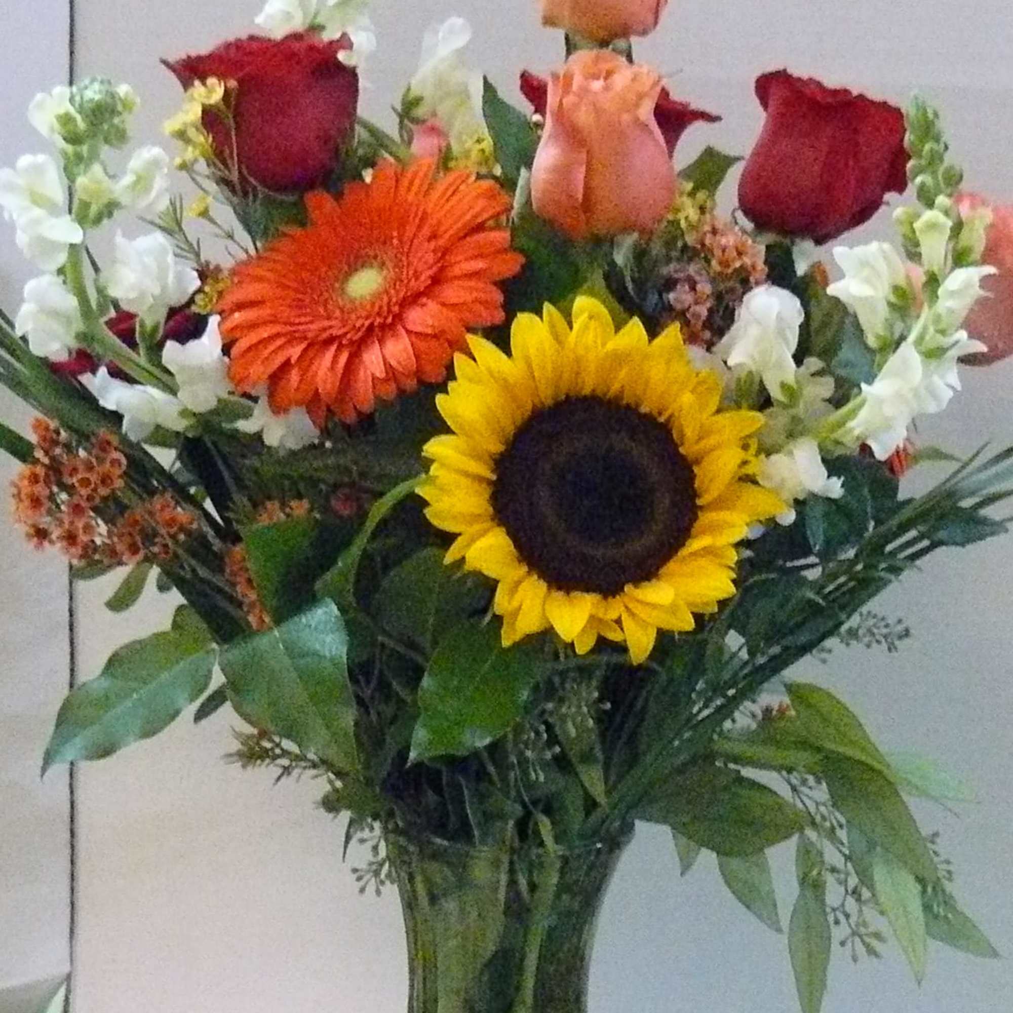 Mixed bouquet of roses, gerbera daisies, and sunflowers in a glass vase