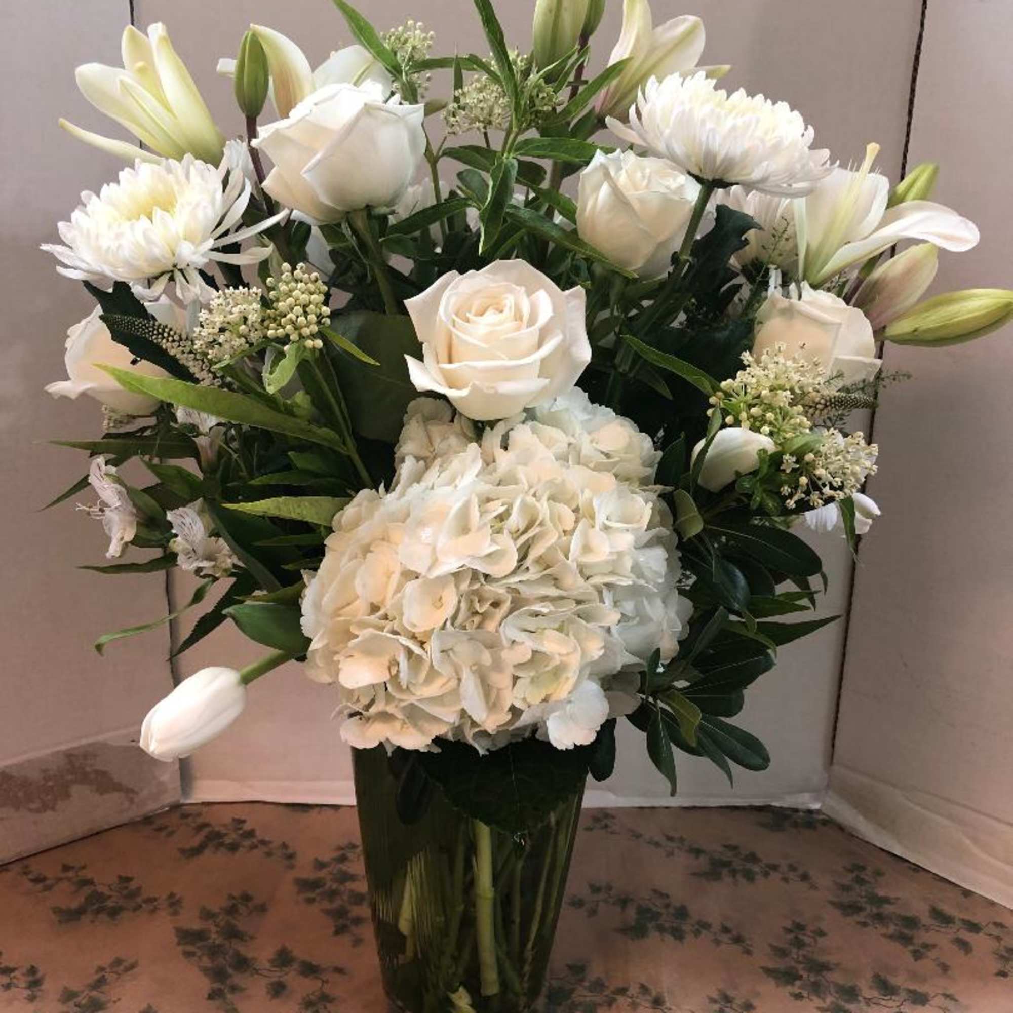 White roses, hydrangea, and lilies arranged in a tall glass vase