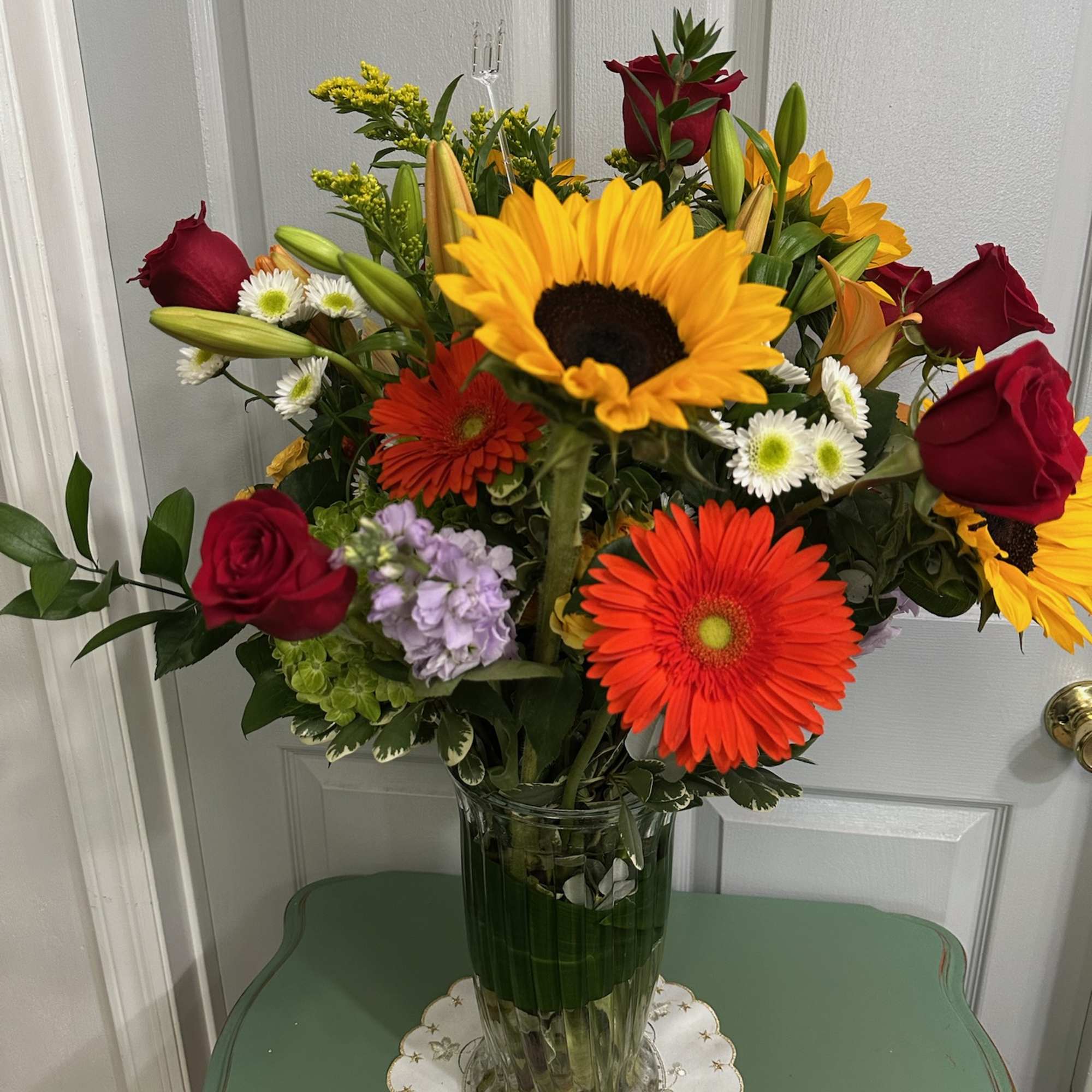 Mixed bouquet of sunflowers, red roses, and orange gerbera daisies in a glass vase