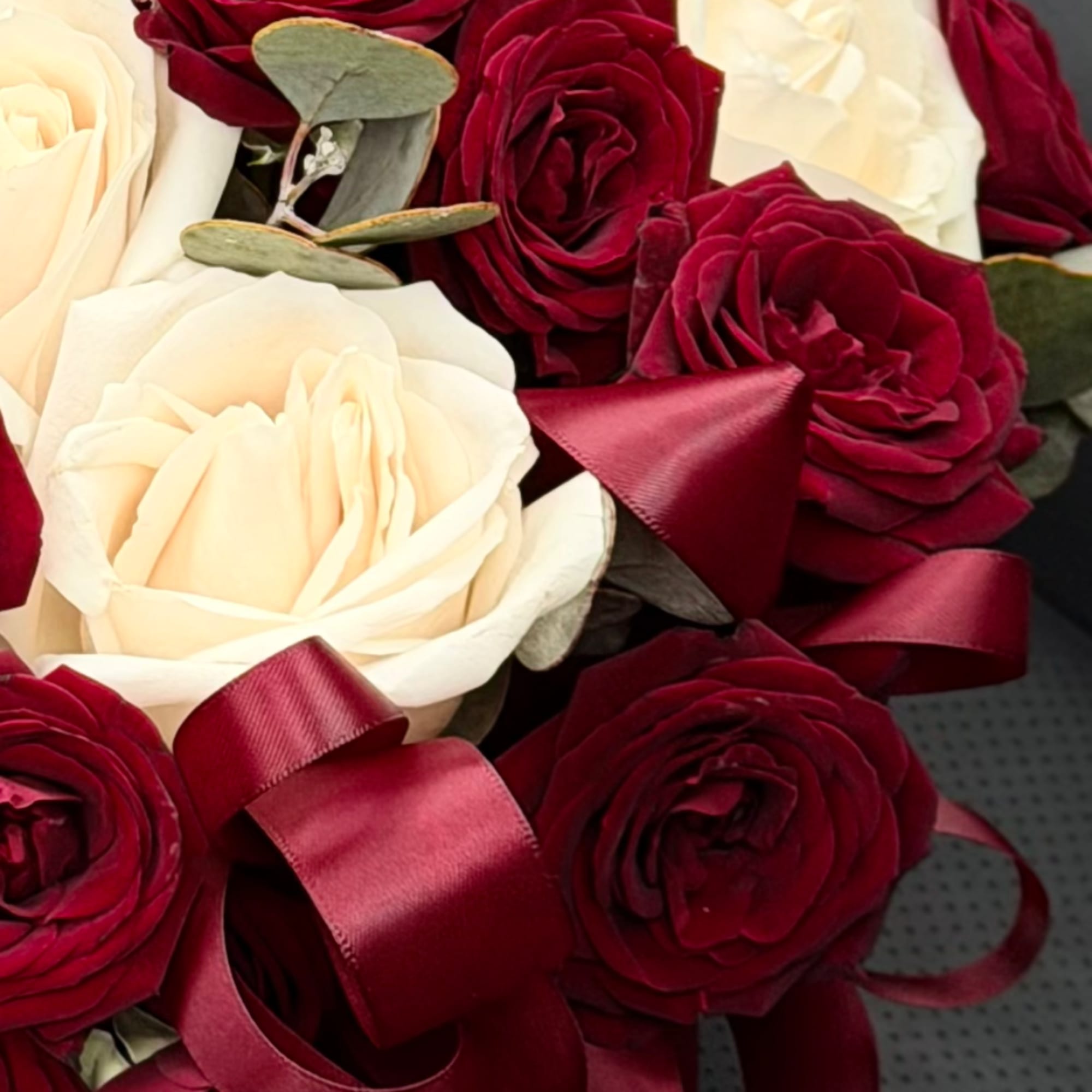 Close-up bouquet of cream and deep red roses with burgundy ribbon