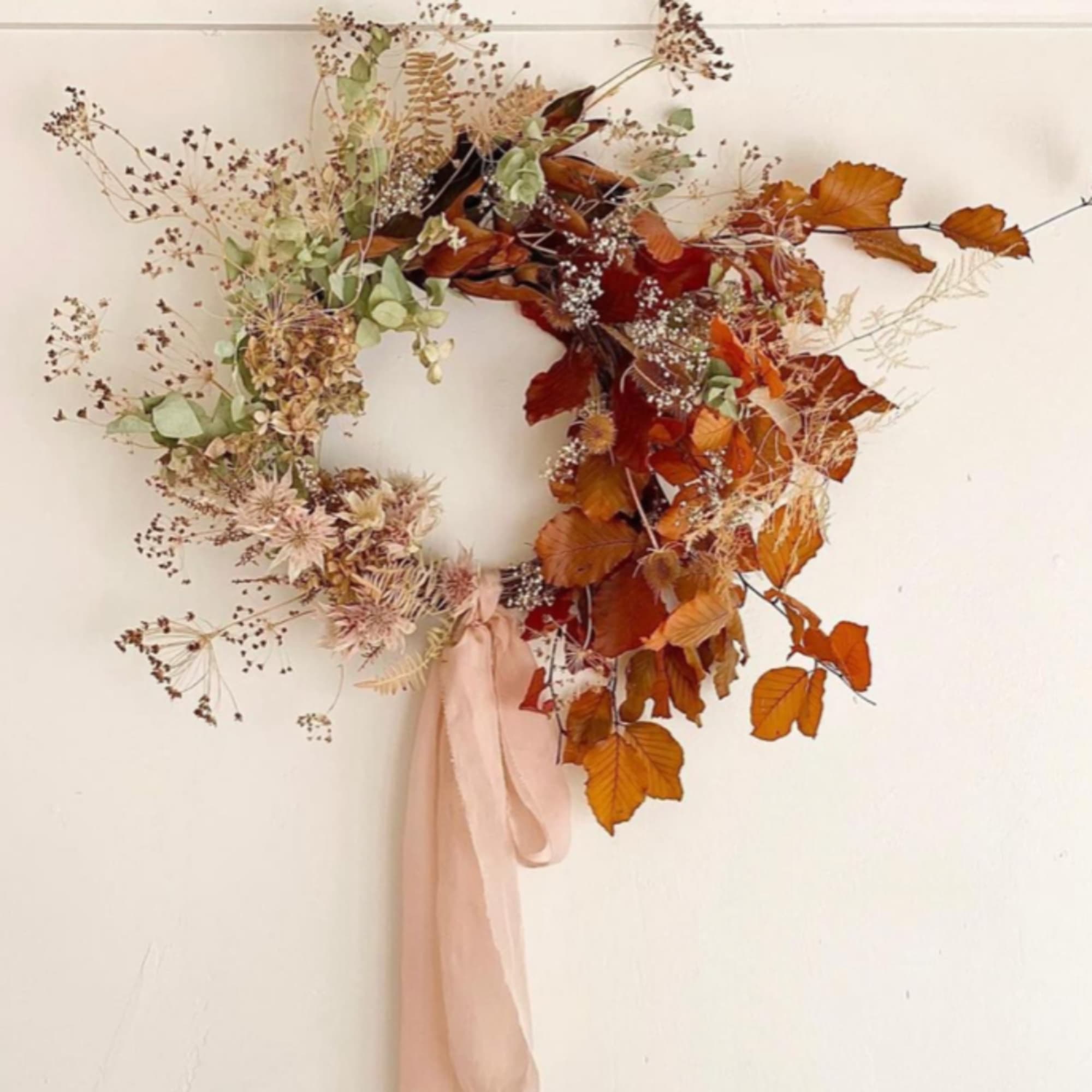 Autumn floral wreath with dried flowers and orange leaves, tied with a blush ribbon