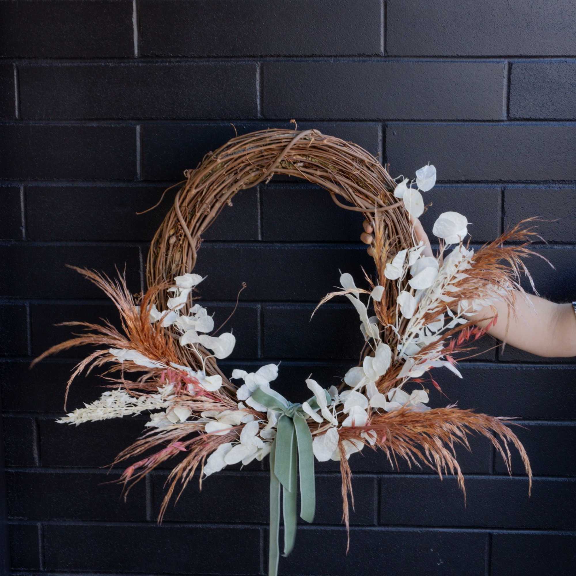 Asymmetrical dried floral wreath with white accents and sage ribbon on a grapevine base.