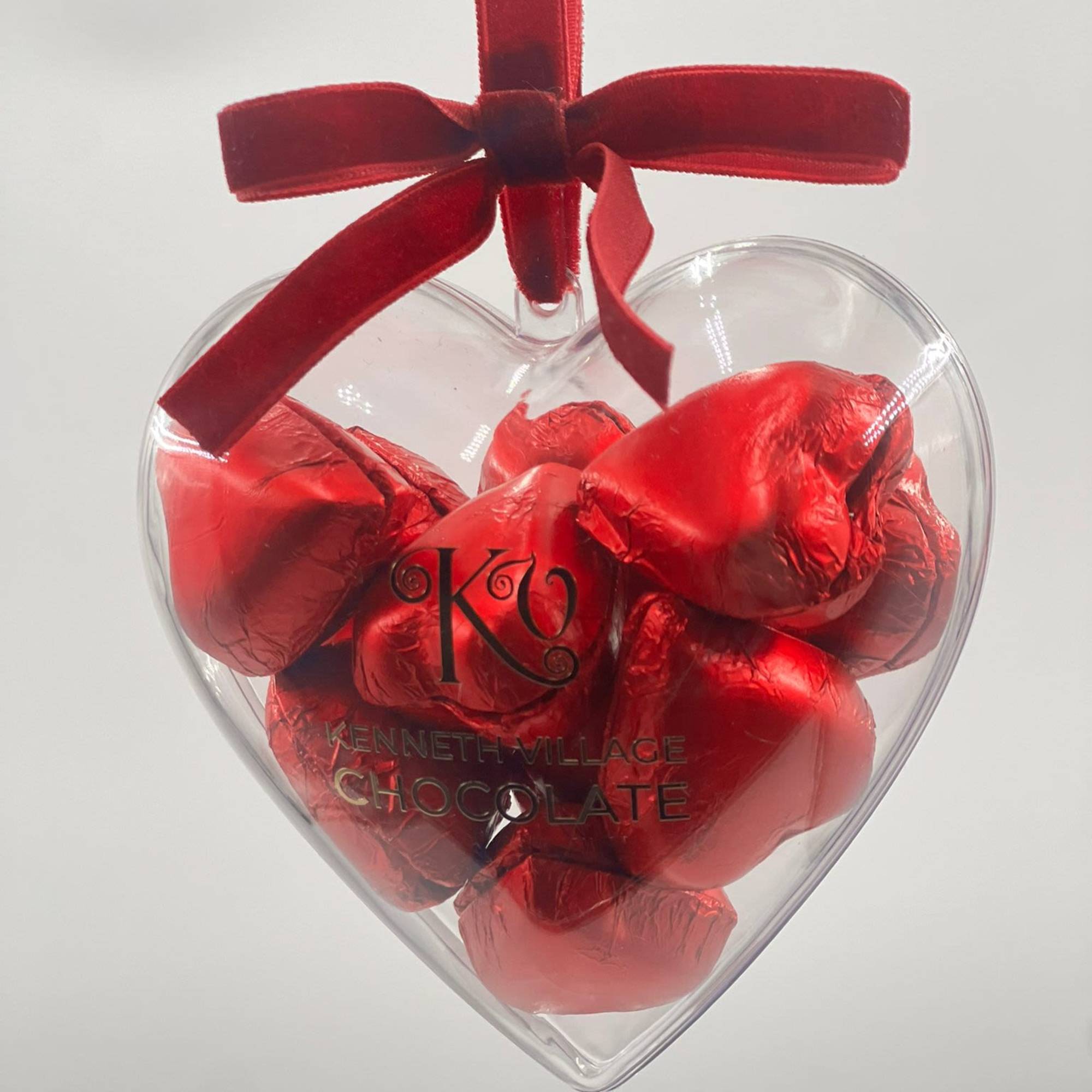 Heart-shaped box of red foil-wrapped chocolates with a red ribbon bow