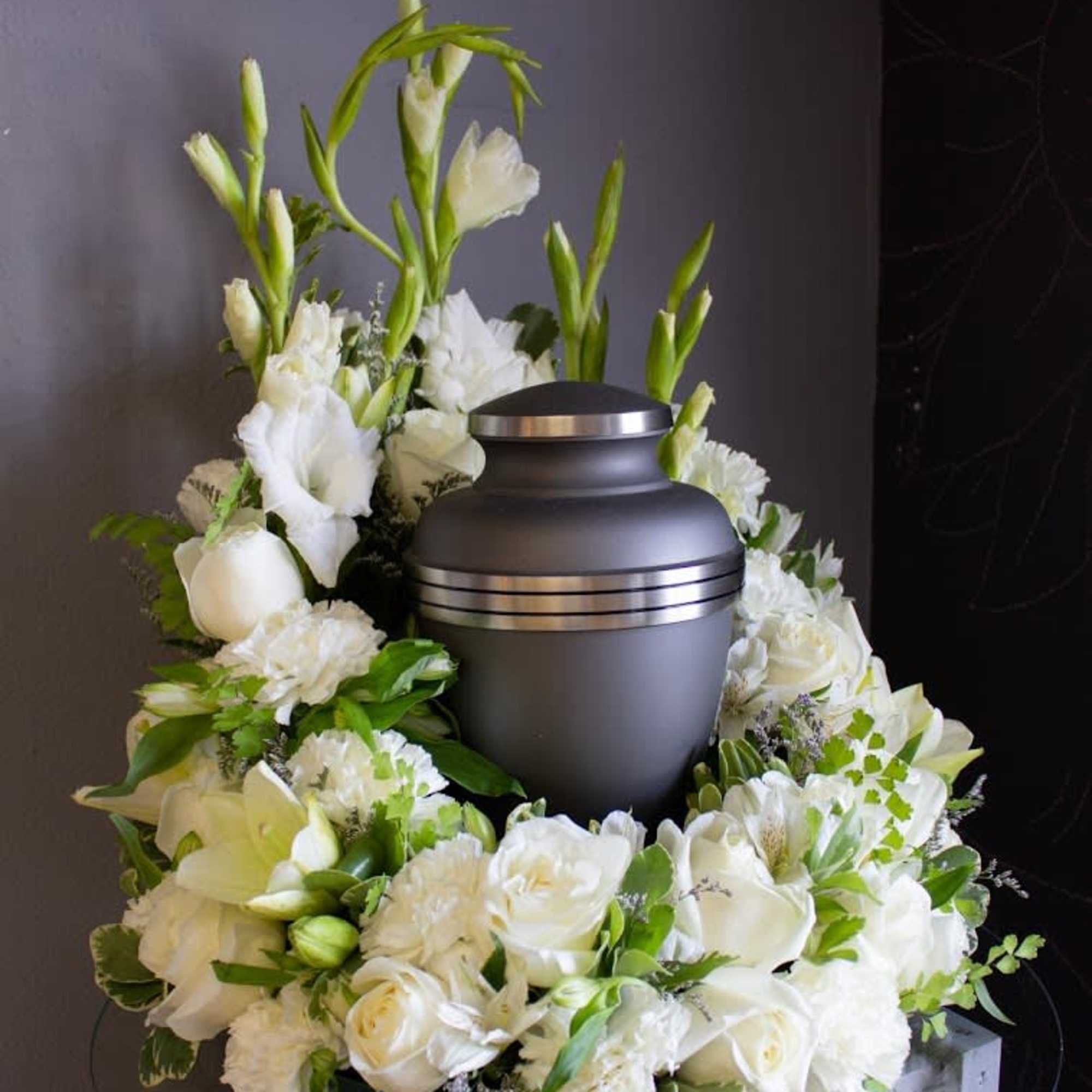Cremation urn encircled by a wreath of white flowers on a glass table