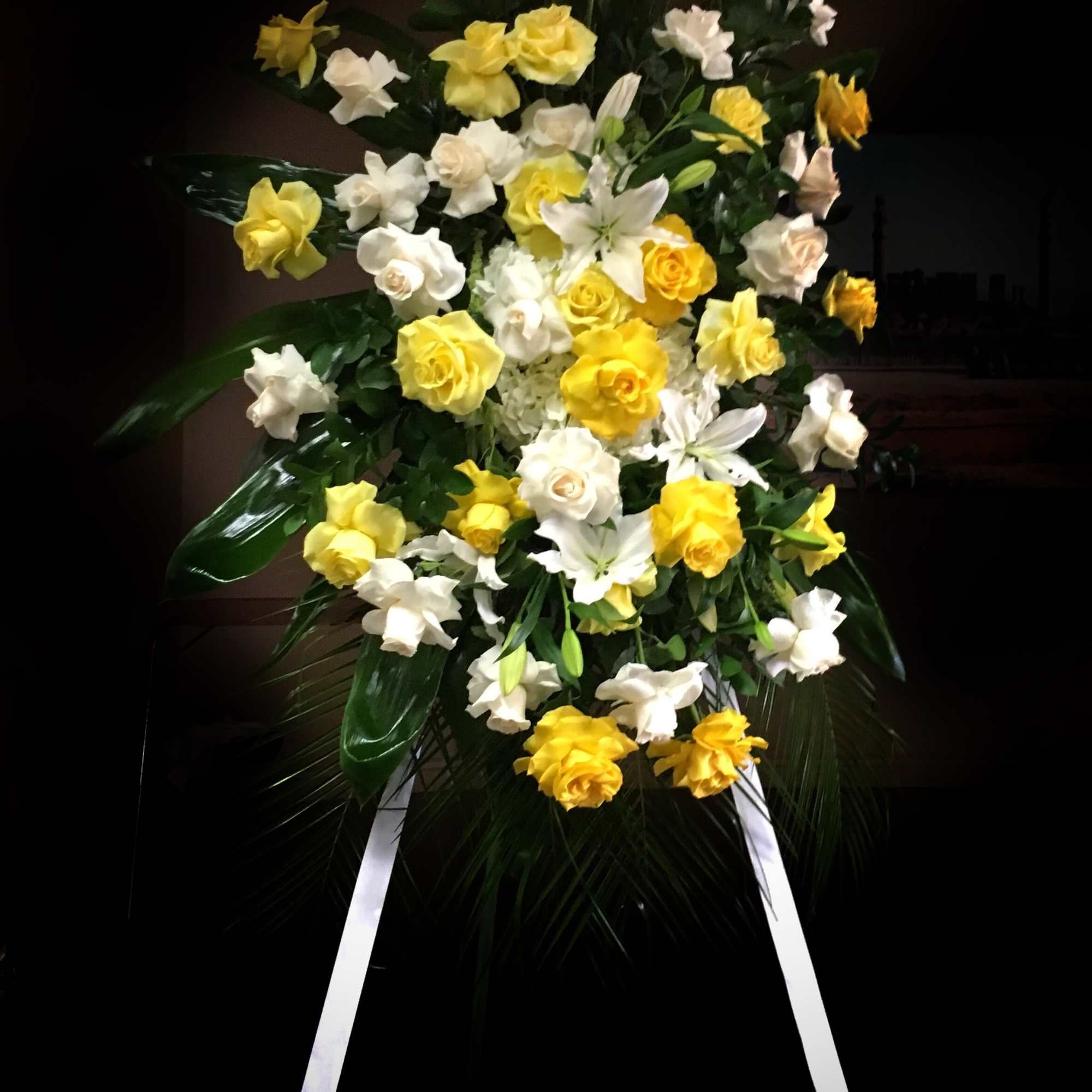 Standing floral spray of yellow and white roses with lilies on an easel