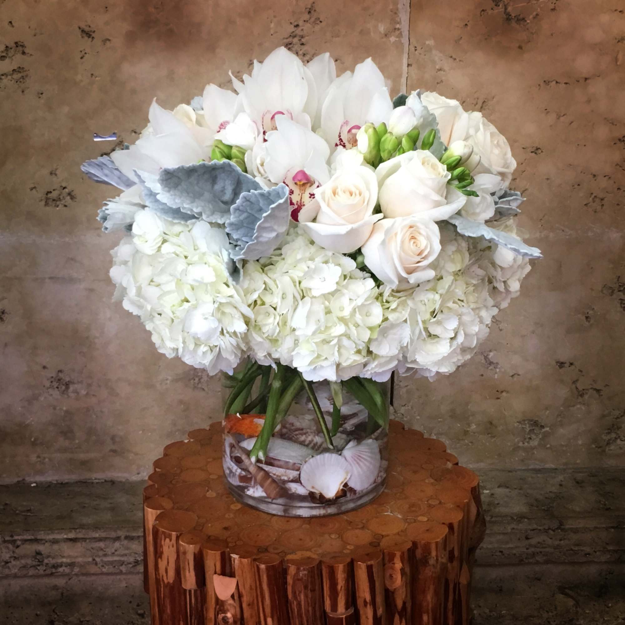 White floral arrangement in a clear glass vase with roses and orchids
